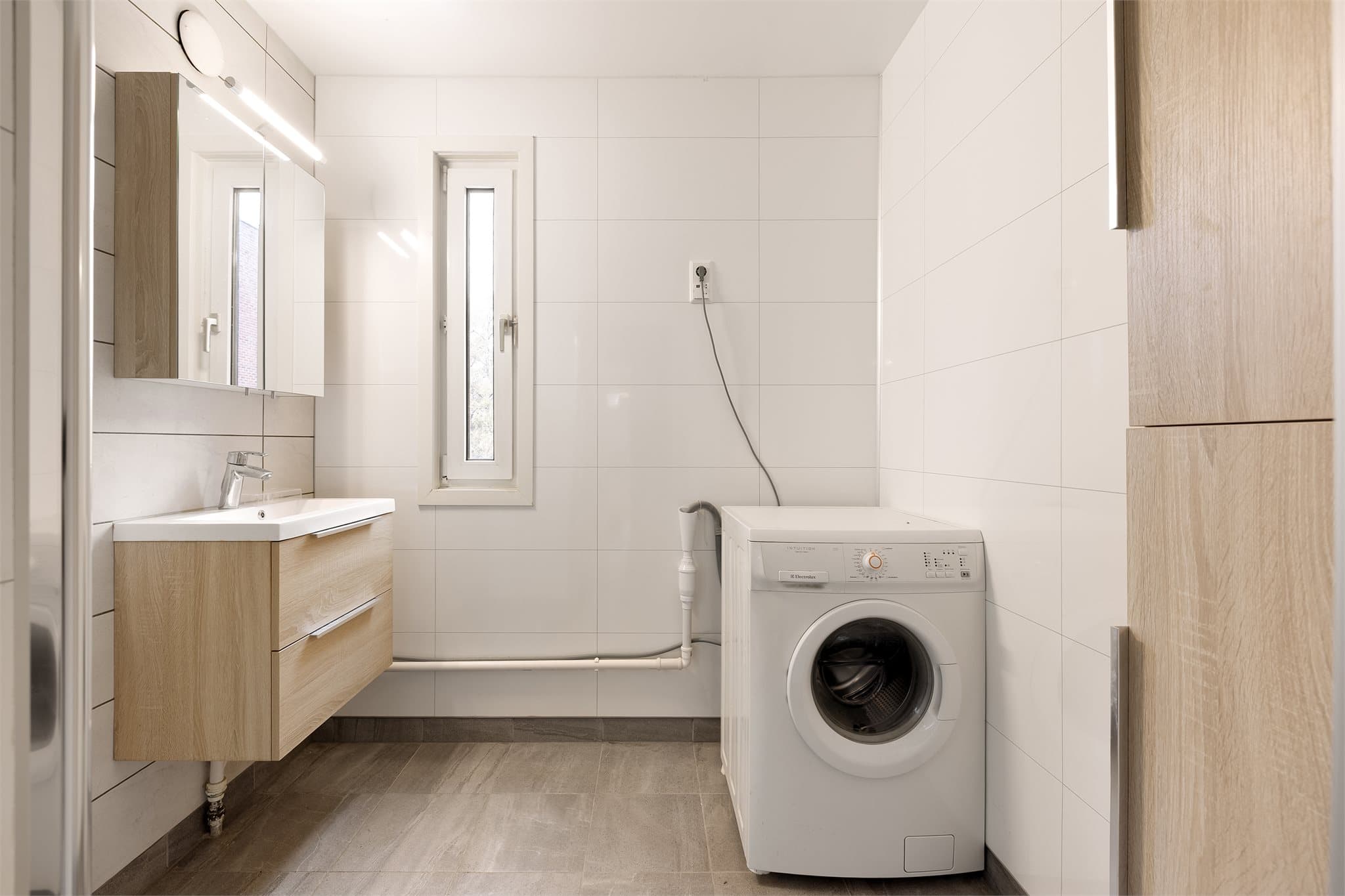 Moderne baderom med servantinnredning, skap, dusjhjørne og opplegg for vaskemaskin.