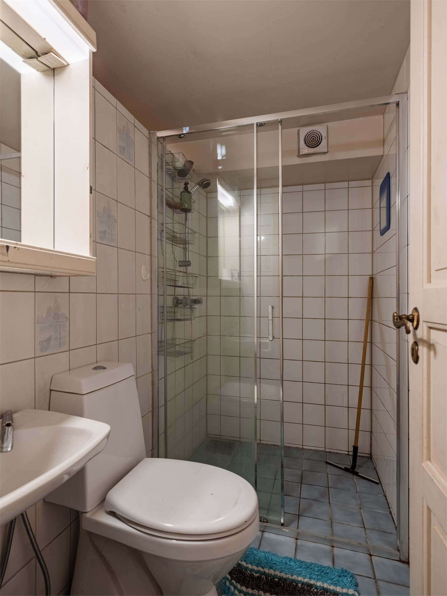 Badet i underetasjen er av eldre dato, med fliser på gulv og vegger, dusj, klosett og servant.