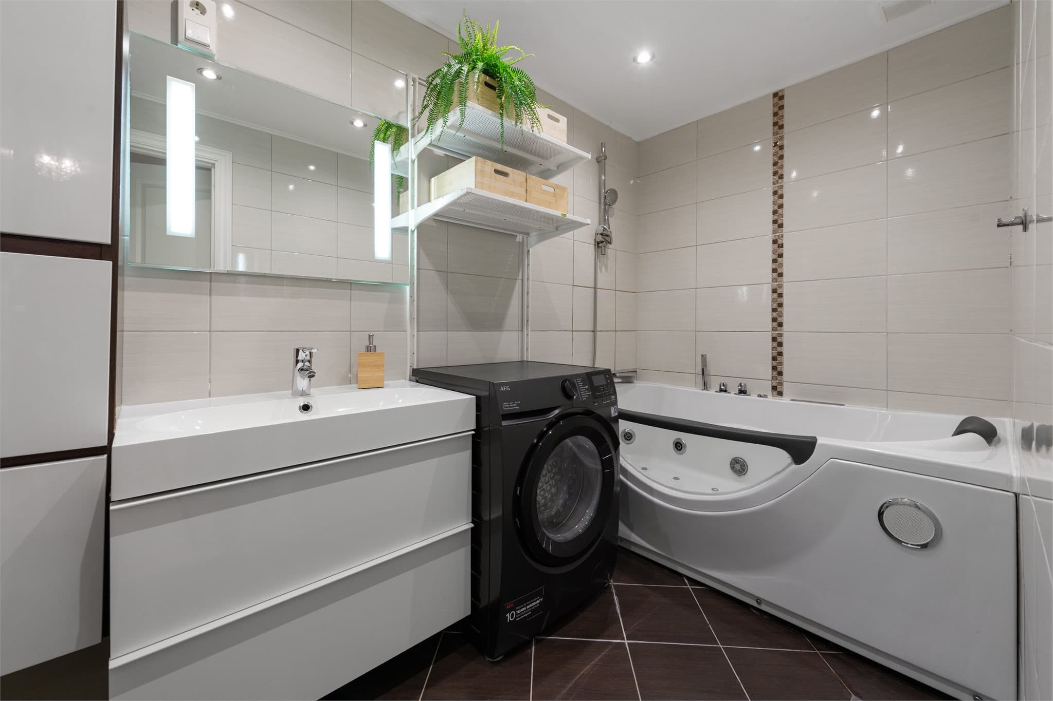 Flislagt bad med badekar og lys og moderne baderomsinnredning