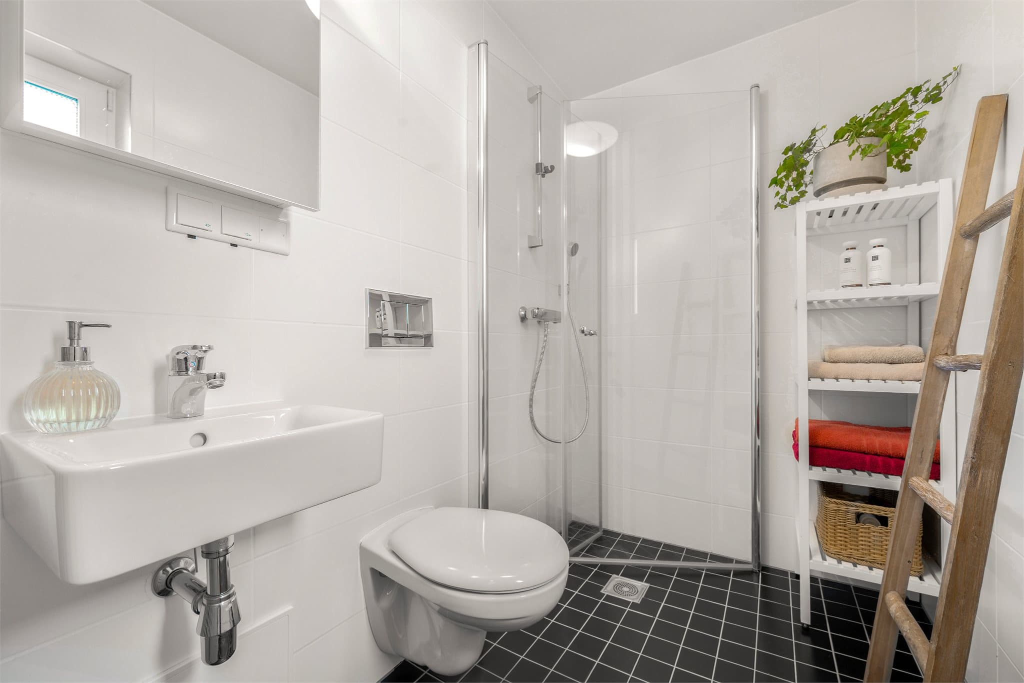 Leiligheten disponerer også et stilrent og funksjonelt baderom nummer to, praktisk plassert med adkomst fra gangen. Rommet er innredet med moderne, tidløse materialvalg og har dusjhjørne med glassvegger, vegghengt toalett og servant.