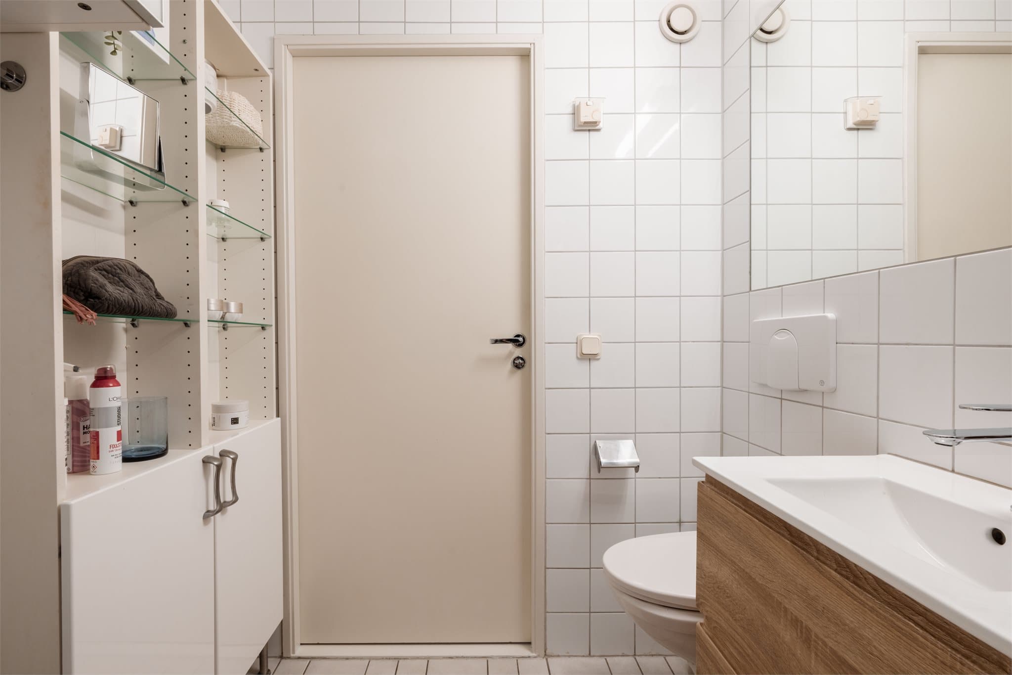 Badet har veggmontert toalett og servantskap for oppbevaring.