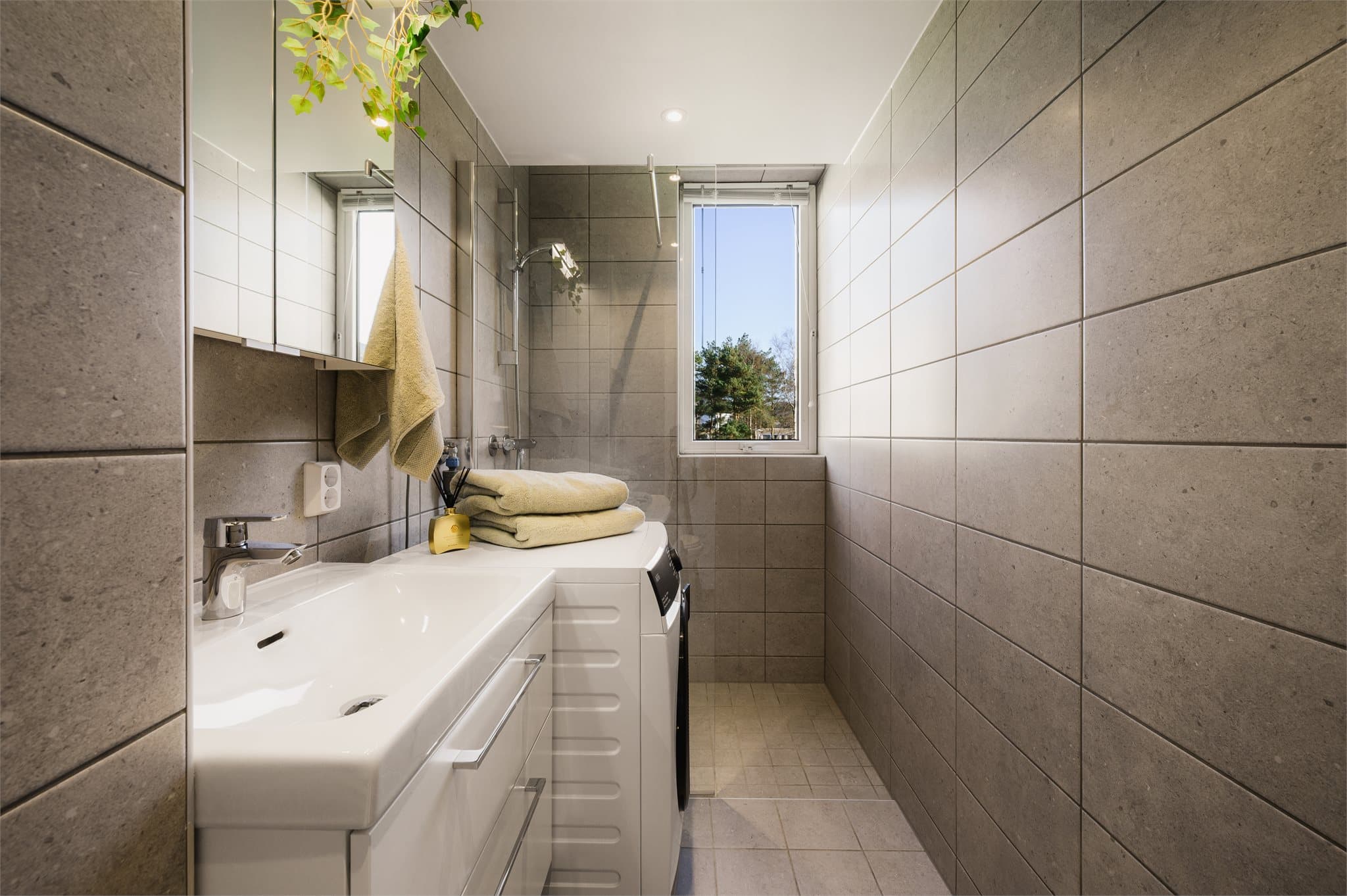 - Leilighetens bad er innredet med heldekkende servant, veggmontert toalett, dusjsone med glassvegg og opplegg for vaskemaskin -