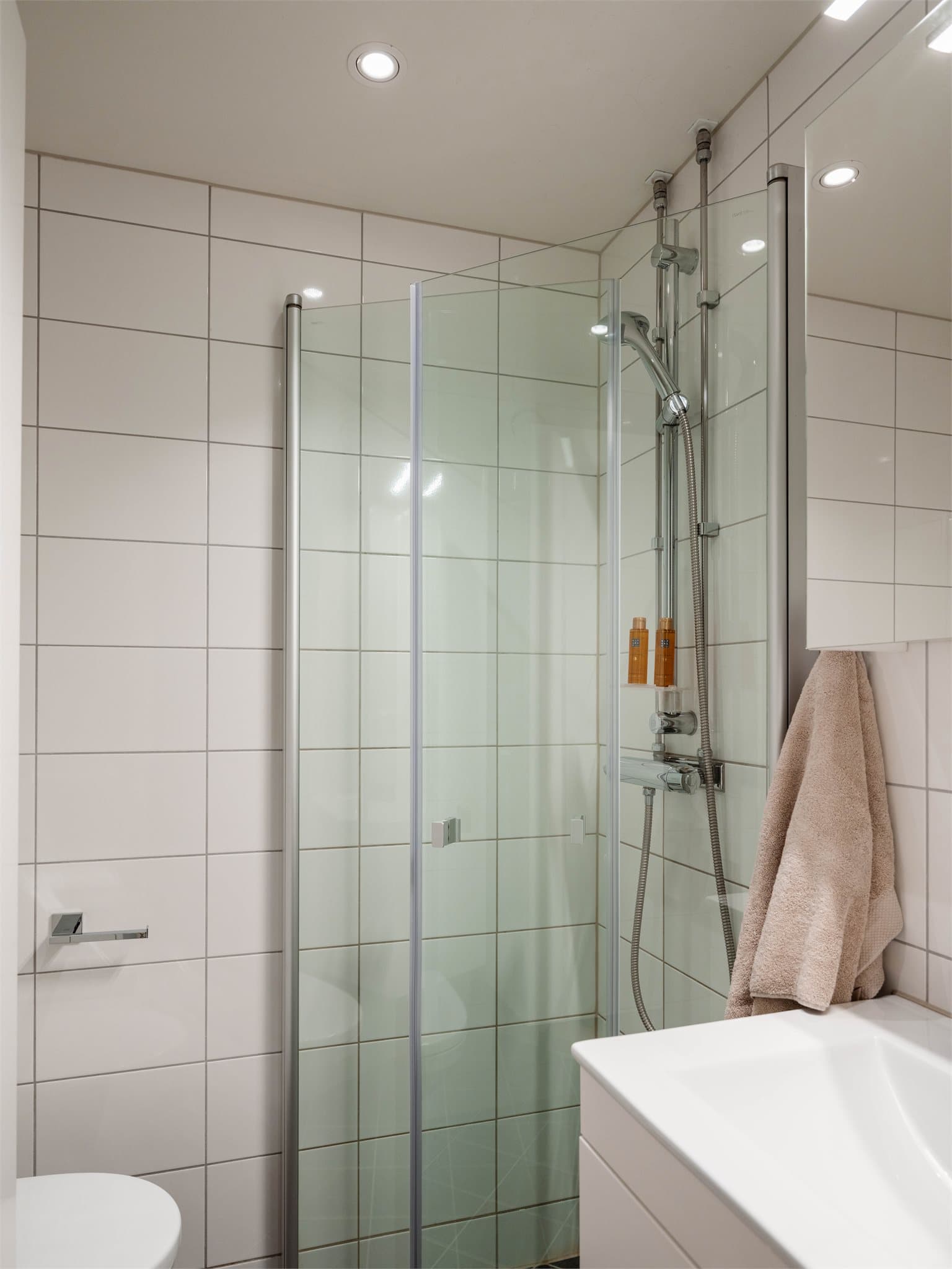 Badet er utstyrt med vegghengt klosett og et dusjhjørne med svingbare glassdører.