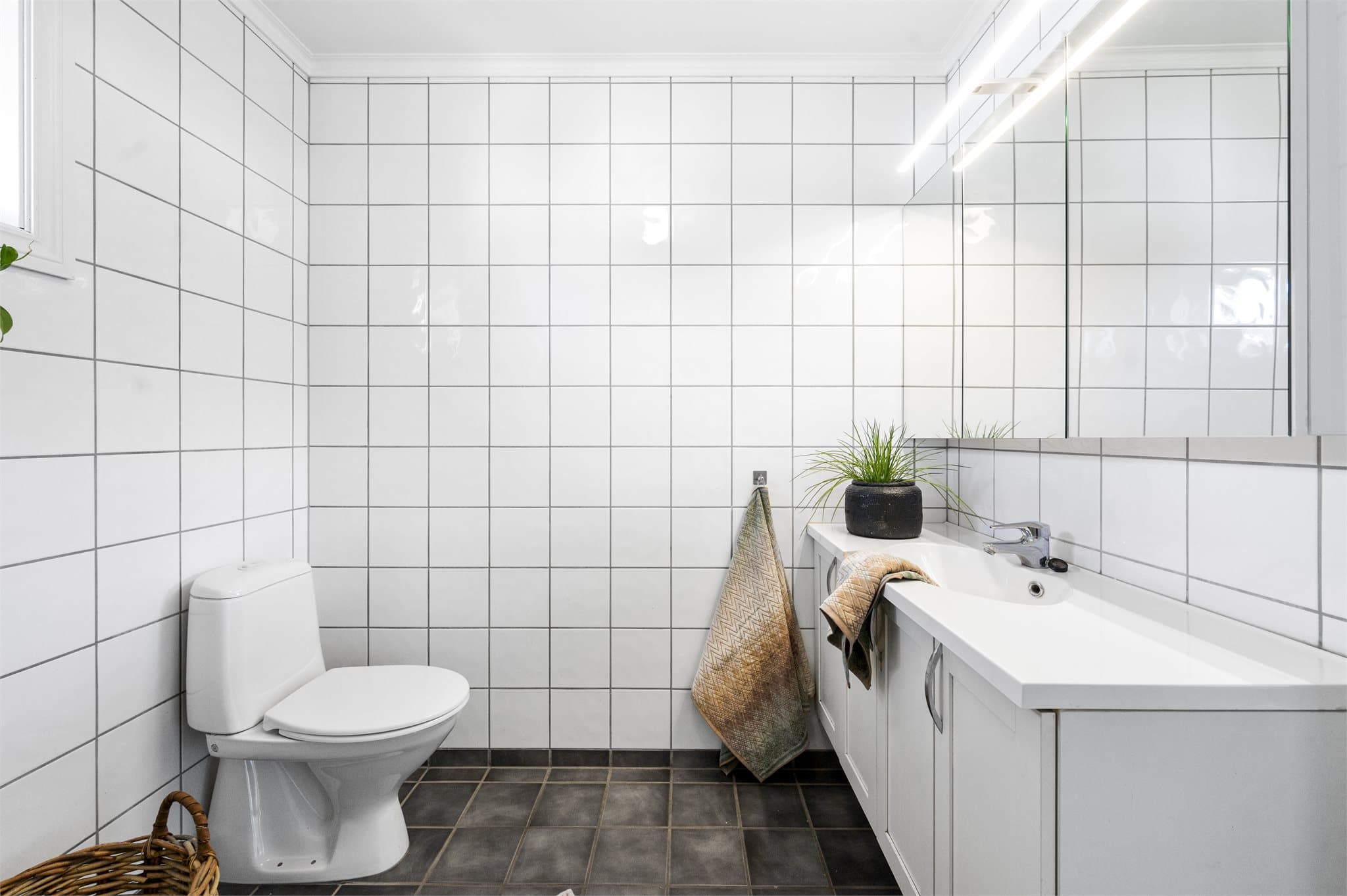 Hvit servant med skapinnredning og speil med lys over.