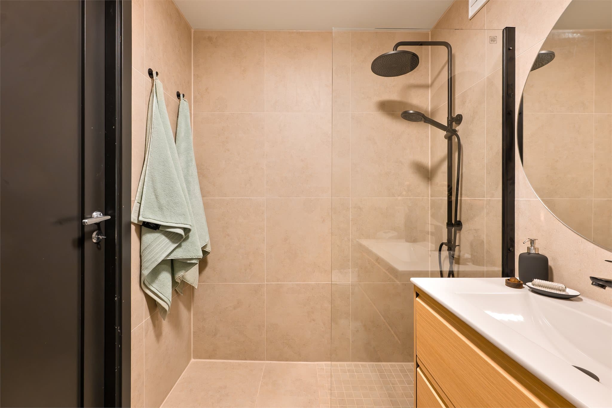 Rommet er innredet med servant med glatte, folierte fronter og heldekkende servant. Det er speil på vegg over servant. Videre har rommet gulvmontert toalett og dusjhjørne med glassfelt, regnfallsdusj, håndholdt dusj og termostatstyrt blandebatteri.