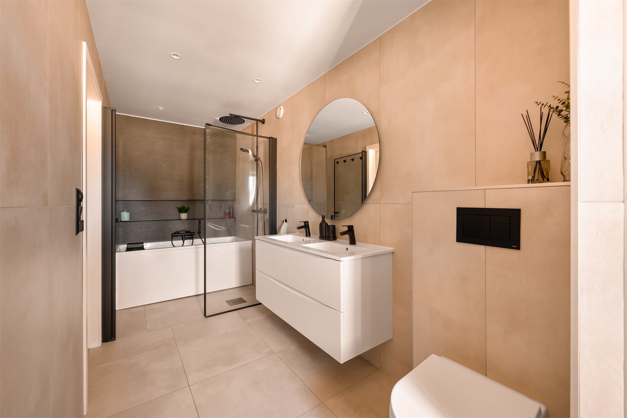 Rommet er innredet med servantskap, speil med belysning på vegg, veggmontert toalett, dusjhjørne, samt badekar med håndholdt dusj.