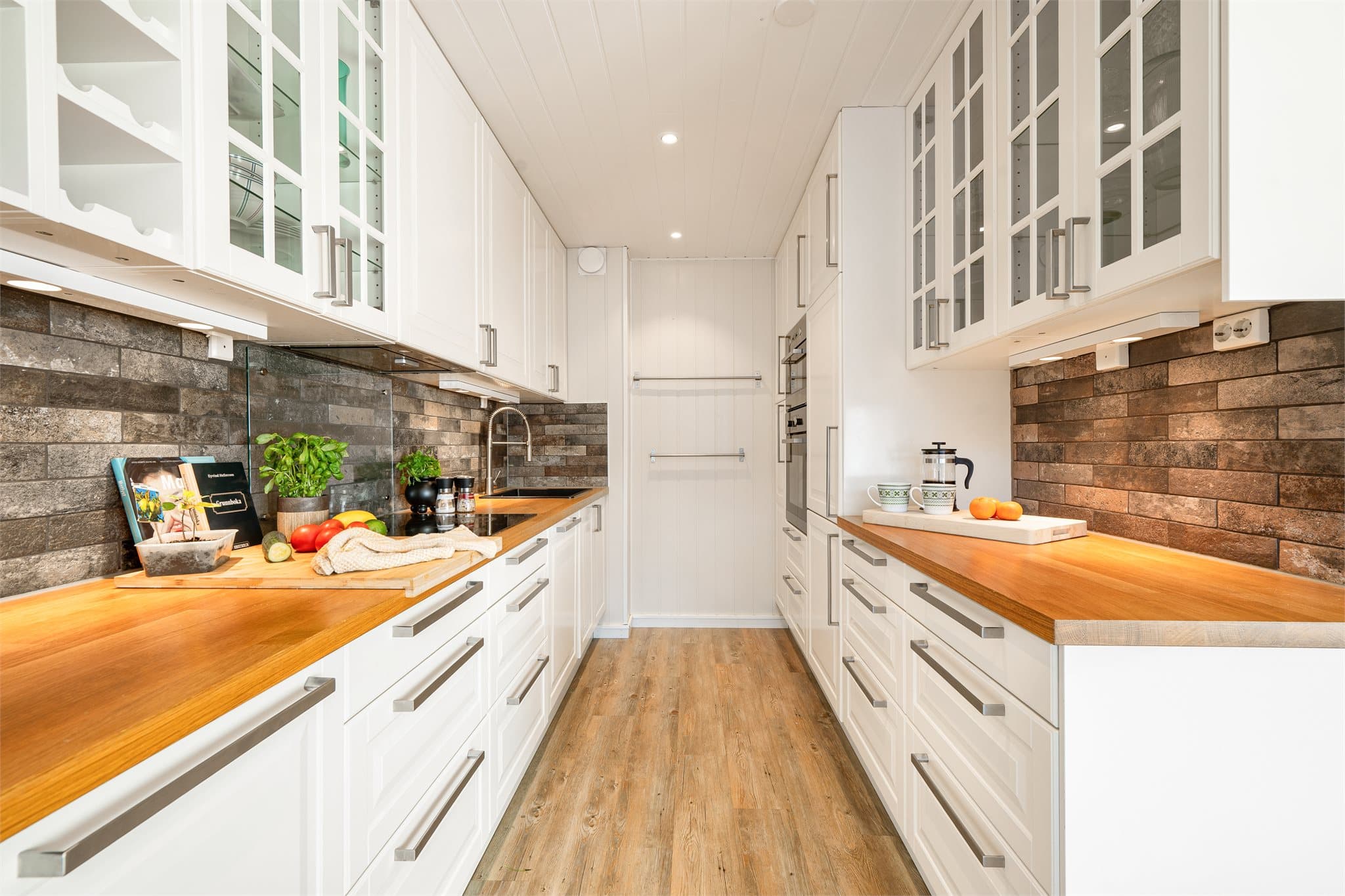 Kjøkkenet er godt opplyst med utstrakt bruk av downlights som skaper en behagelig og funksjonell arbeidsbelysning. Integrerte hvitevarer sørger for et rent og gjennomført helhetsinntrykk – et kjøkken som kombinerer praktiske løsninger med tidløs estetikk.