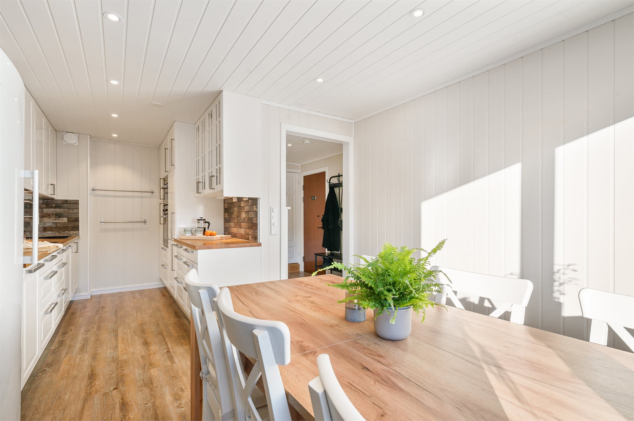 De takhøye skapene sørger for optimal oppbevaring, mens vitrineskapene tilfører både karakter og en luftig følelse. Mellom kjøkkenbenk og overskap finner du dekorative og slitesterke steinfliser som fremhever kjøkkenets kvaliteter.