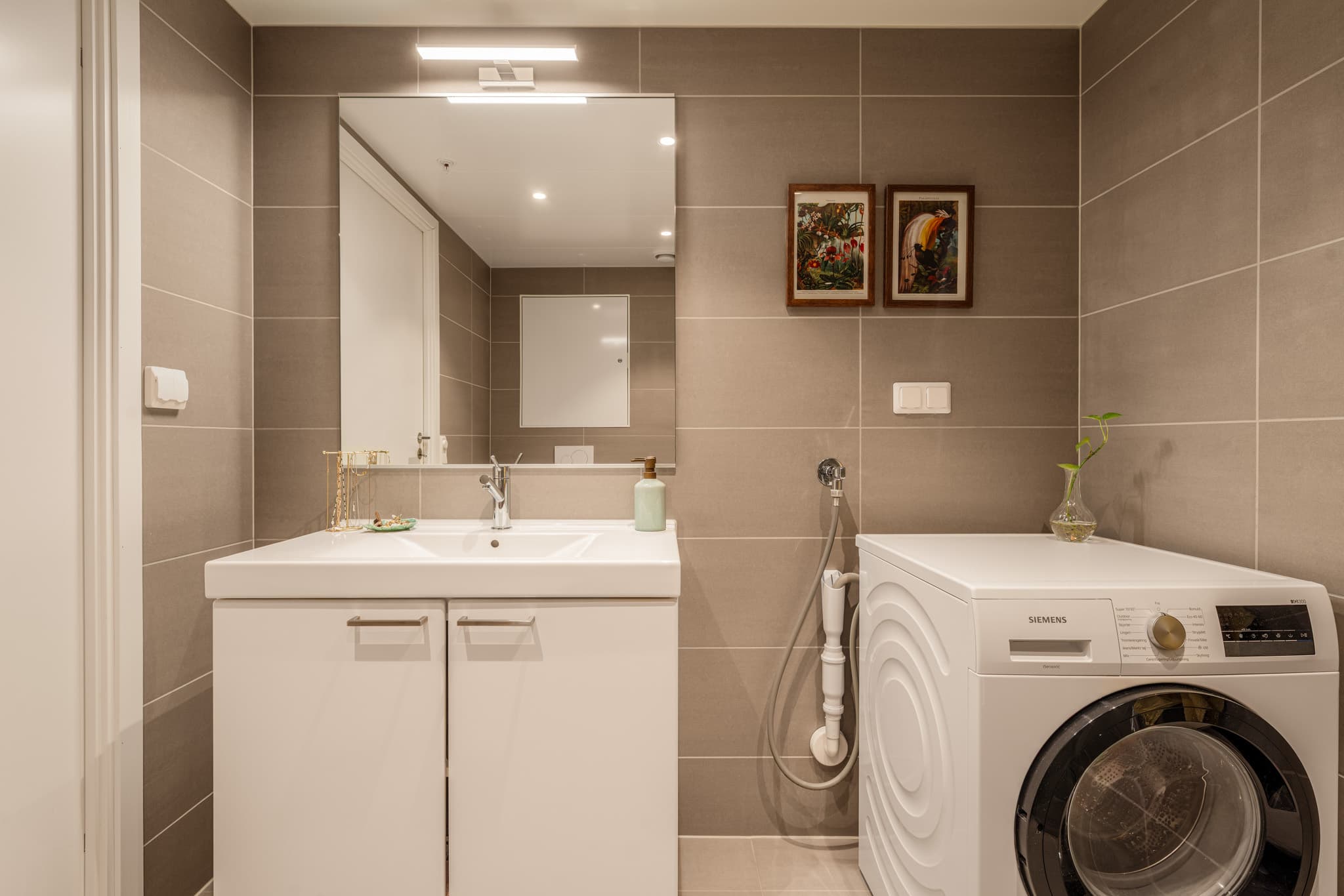 Inredningen består av helservant på skapseksjon, dusjhjørne, vegghengt toalett og opplegg for vaskemaskin.