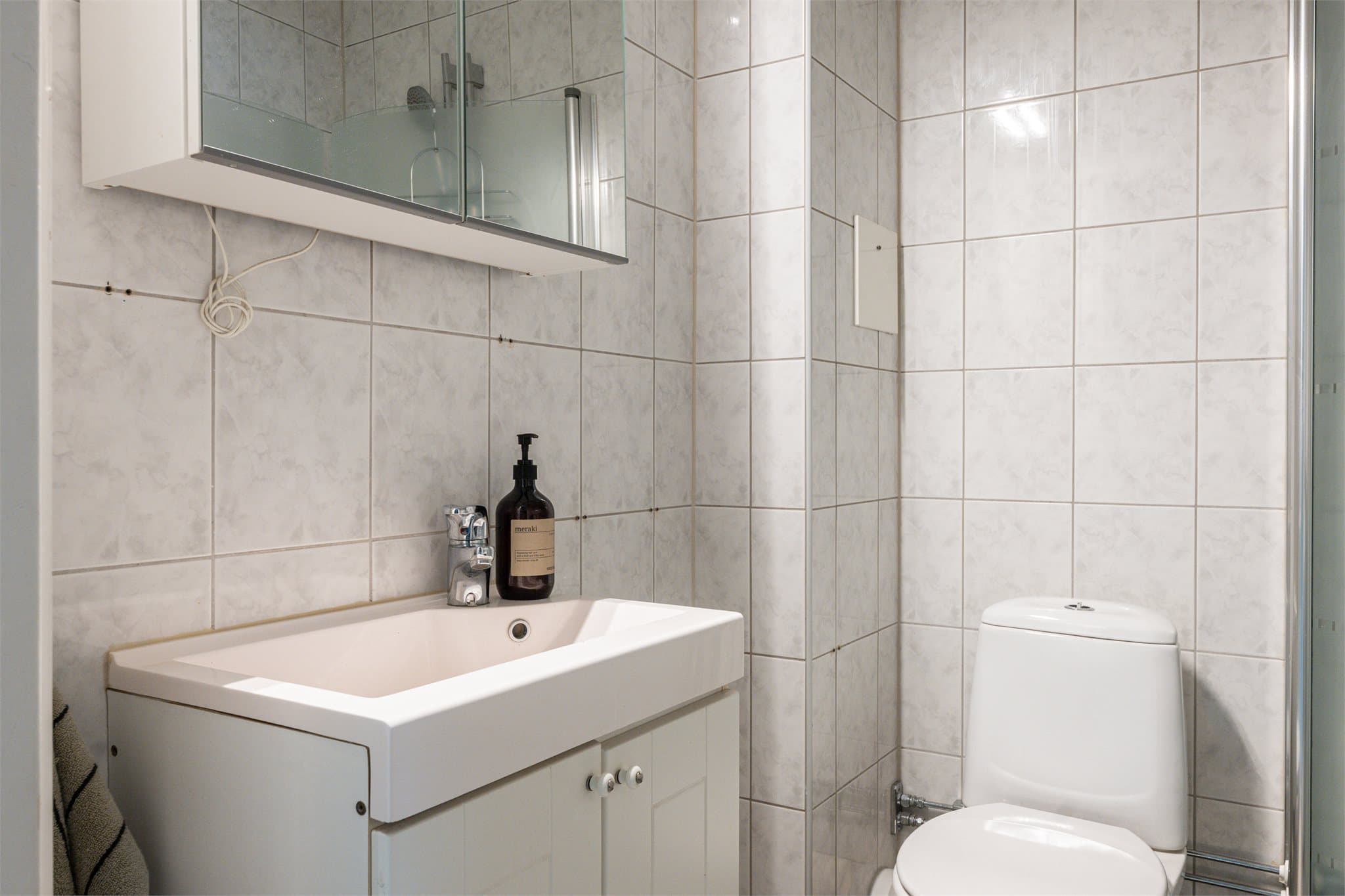 Badet er innredet med servant i baderomsinnredning, toalett og dusjhjørne med svingbare glassdører. Speilskap med belysning over.