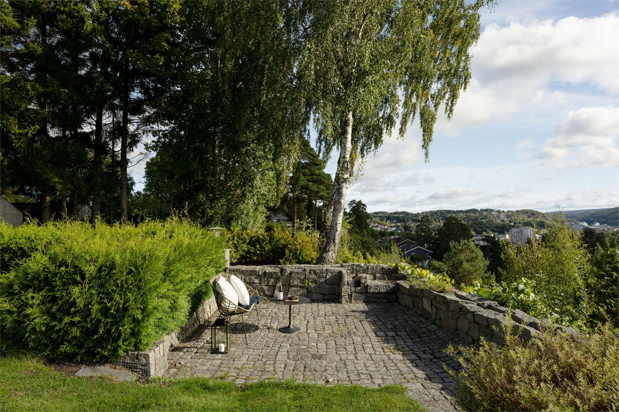 Brosteinsbelagt uteplass rammet inn av natursteinsmur med utsikt mot Halden.