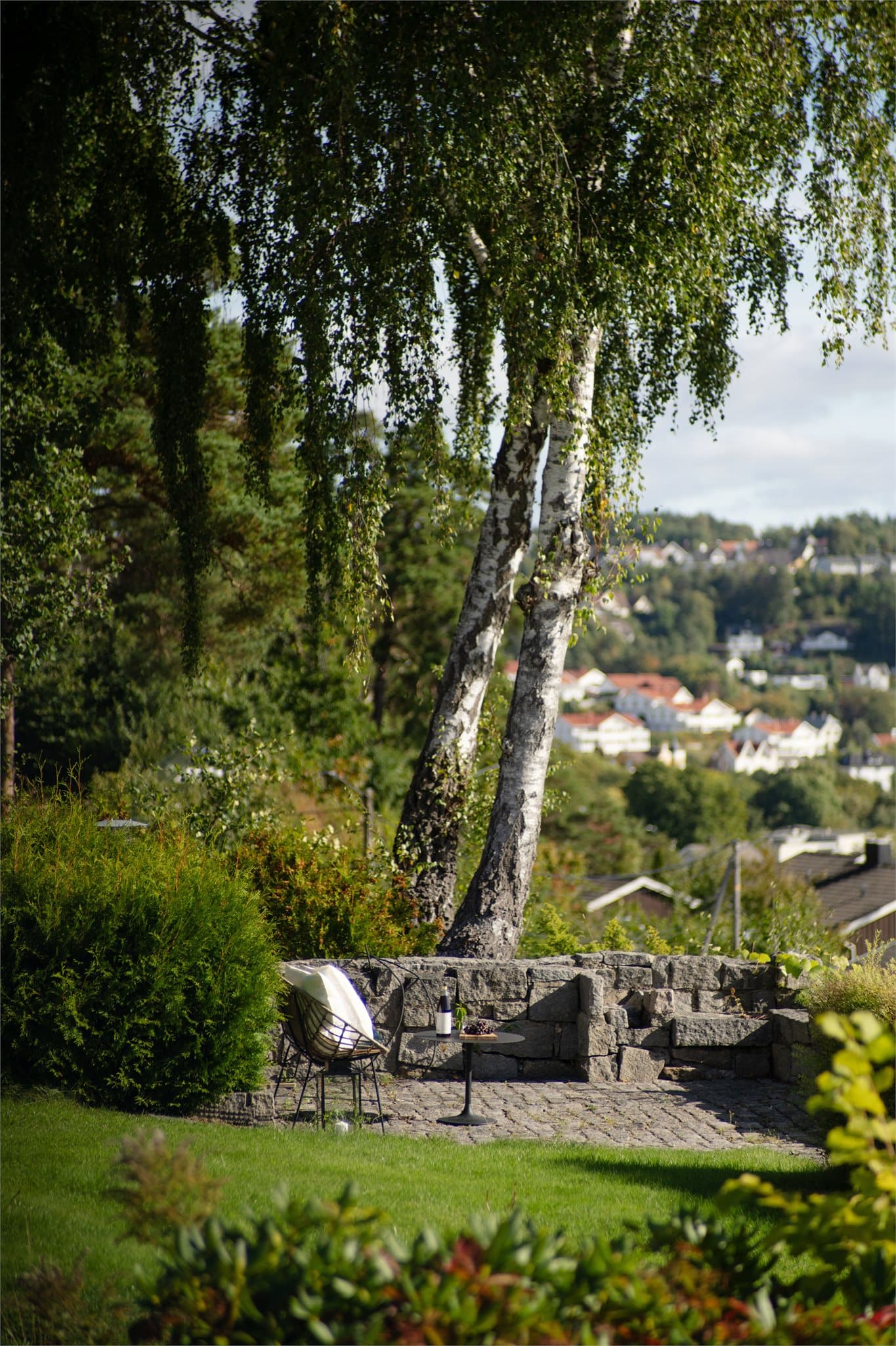 Stemningsfull uteplass skjermet av trær og hekk med utsikt mot byen.