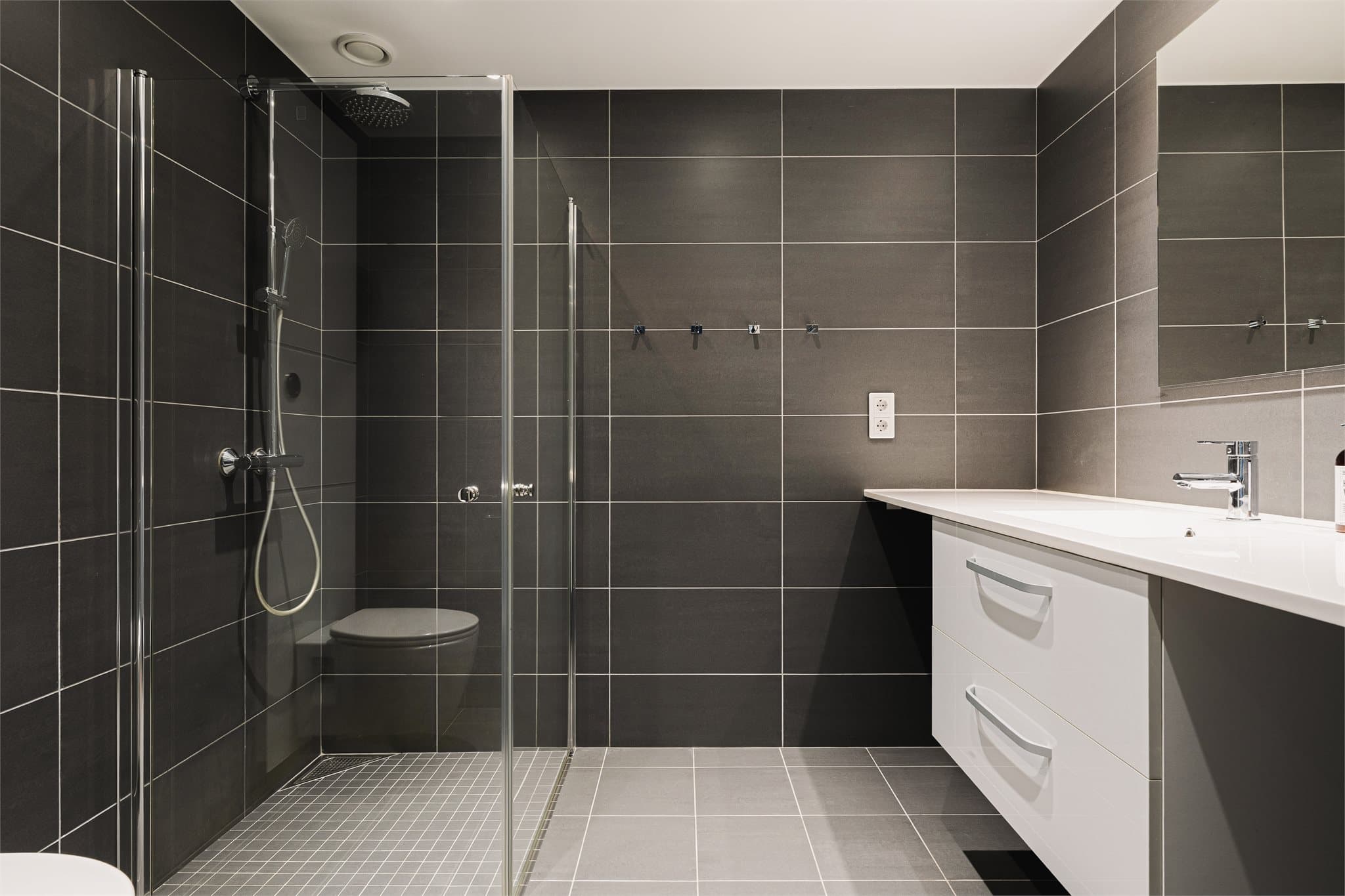 Badet har en innbydende og helhetlig utforming med flislagte overflater og downlights som gir et behagelig lys.