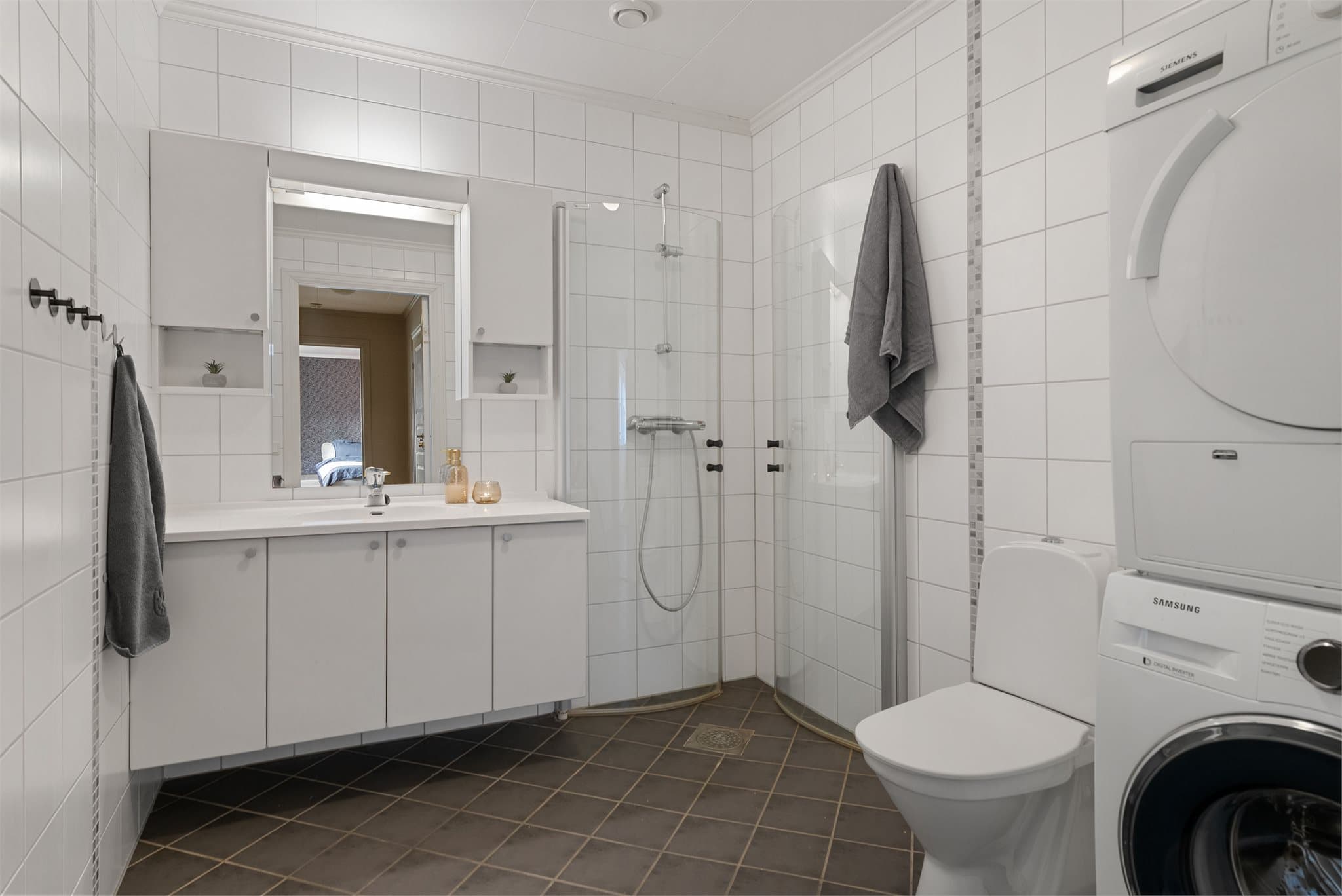 Flislagt bad med dusjhjørne med innfellbare glassvegger, toalett, servantinnredning og opplegg for vaskemaskin.