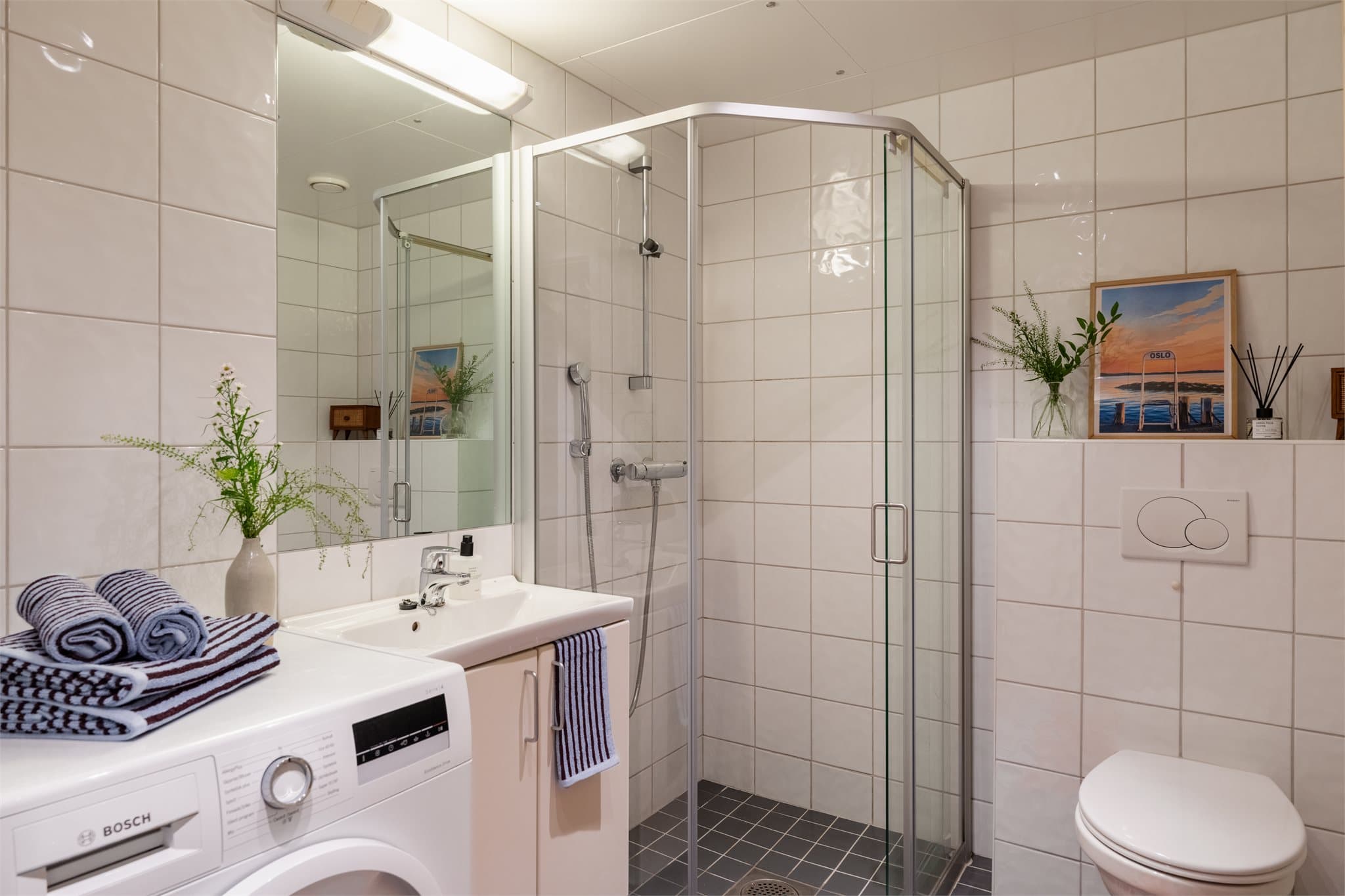 Badet er innredet med vegghengt klosett, servant med innredning, speil med lys og dusjhjørne med svingbare glassdører.