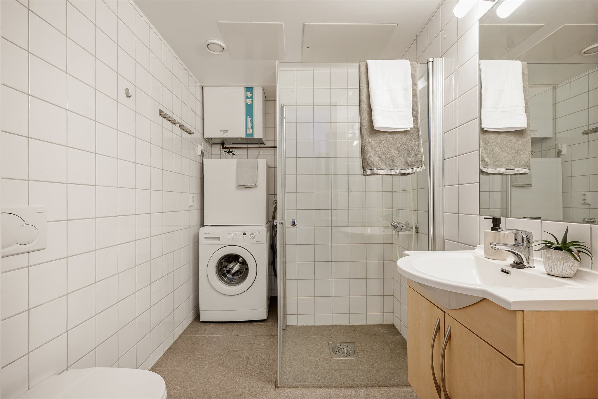Flislagt baderom utstyrt med servantinnredning, toalett og dusjhjørne med innfellbare dusjdører, samt opplegg for vaskemaskin.