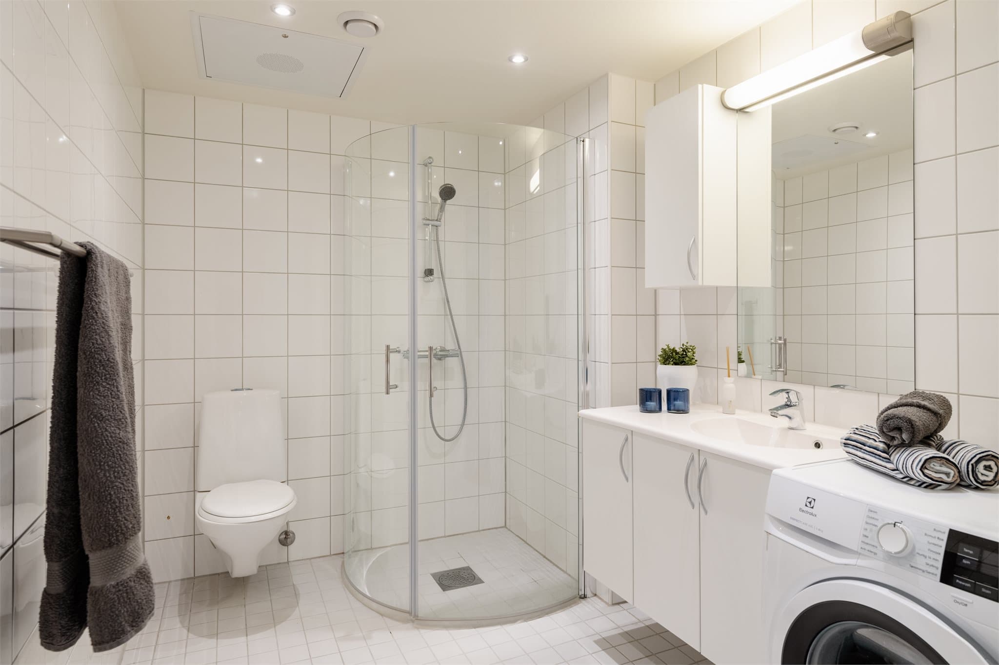 Lyst, helfliset bad fra byggeåret med slette overflater og downlights i himlingen.