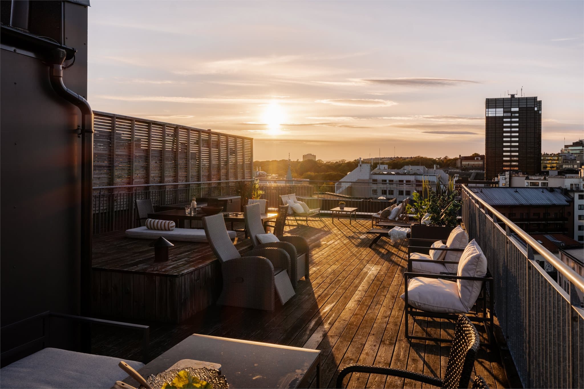 Felles takterrasse med tredekke, flere sittegrupper og vidstrakt utsikt over byen.