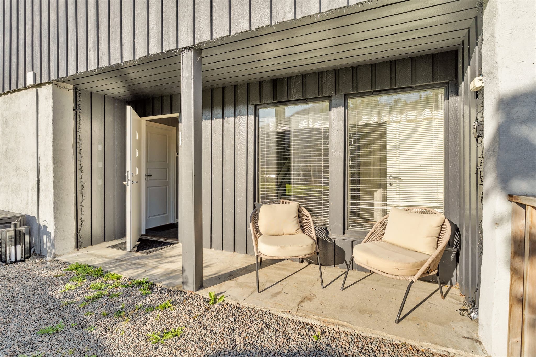 Overbygd inngangsparti med betongdekke og plass til en sittegruppe.