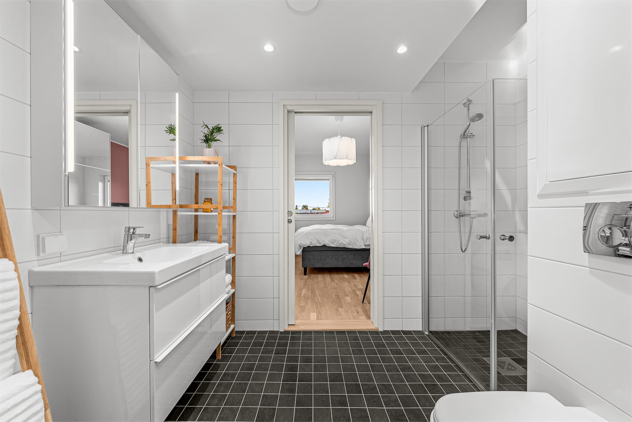 Badet er innredet med helservant på skuffeseksjon, vegghengt toalett og dusjhjørne.