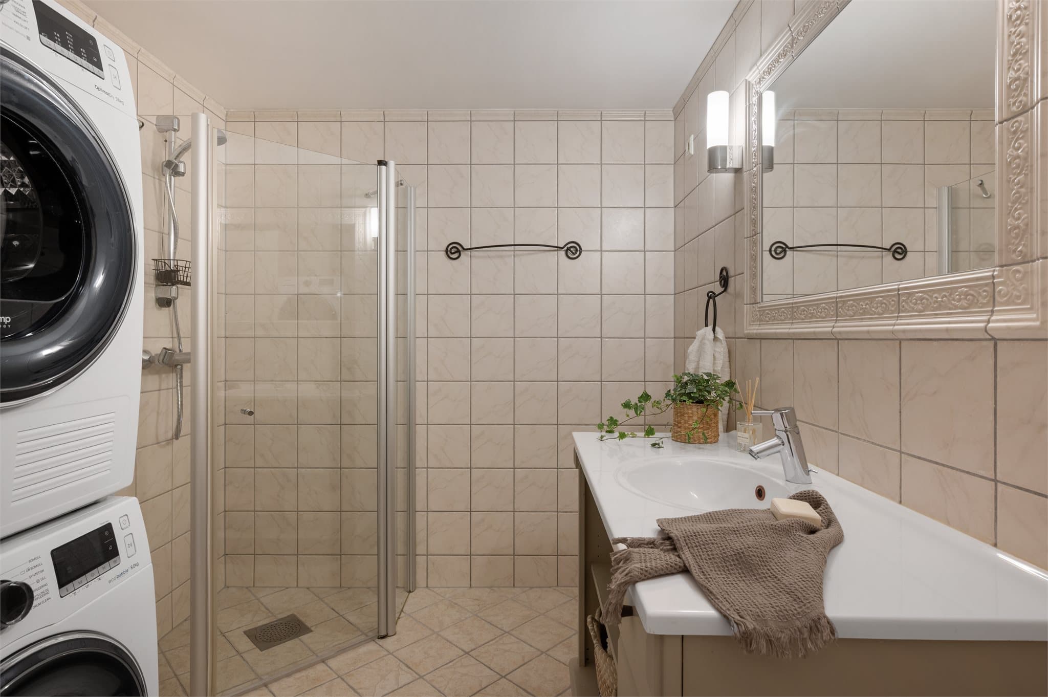- Badet måler 5,8m² og inneholder vegghengt toalett, benkeskap m/ servant, opplegg for vaskemaskin, dusjdør i glass, varmtvannsbereder og fordelerskap til «rør i rør» vannforsyning -