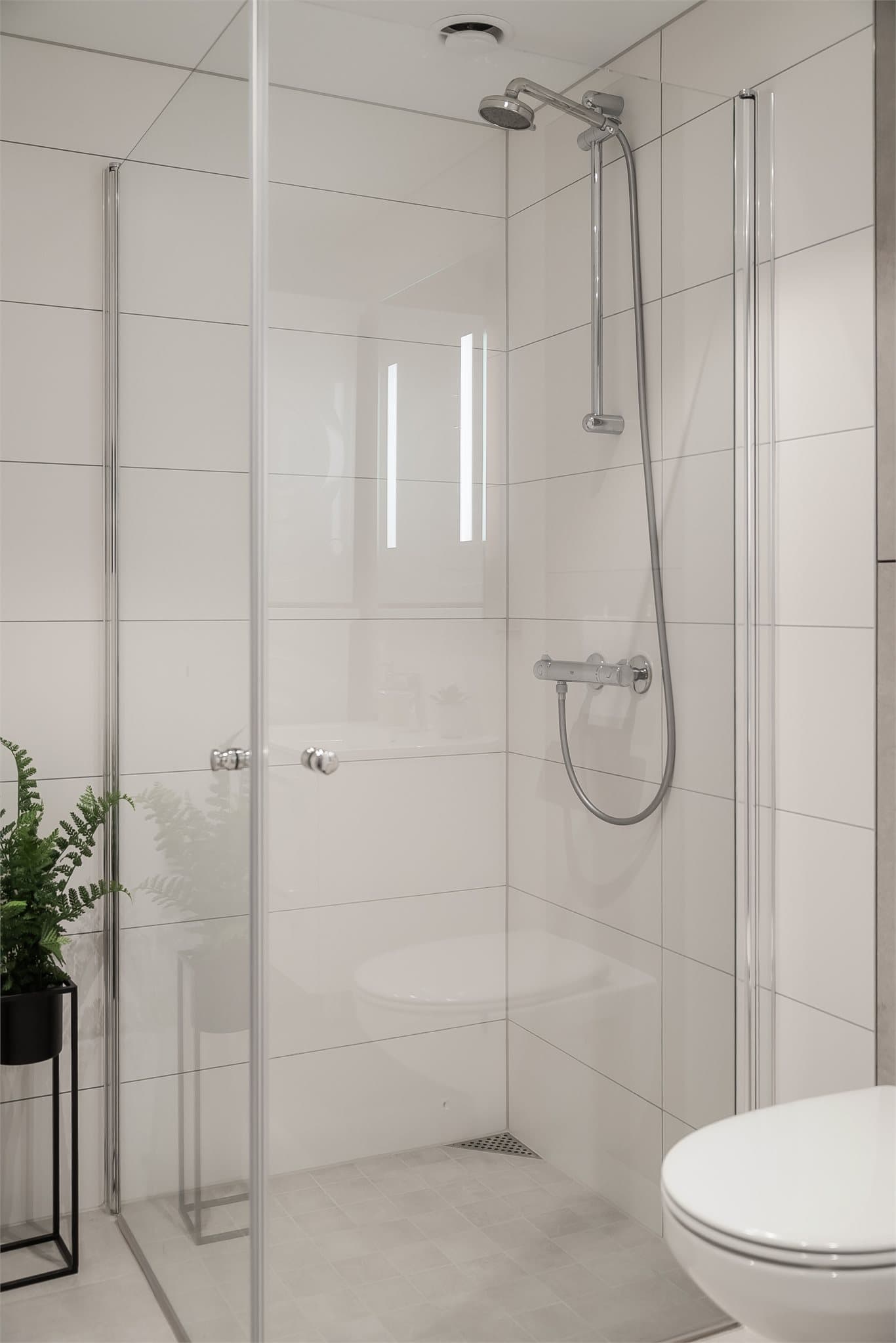 Badet er utstyrt med dusjhjørne med glassvegger og vegghengt toalett, som gir et stilrent og lett uttrykk.