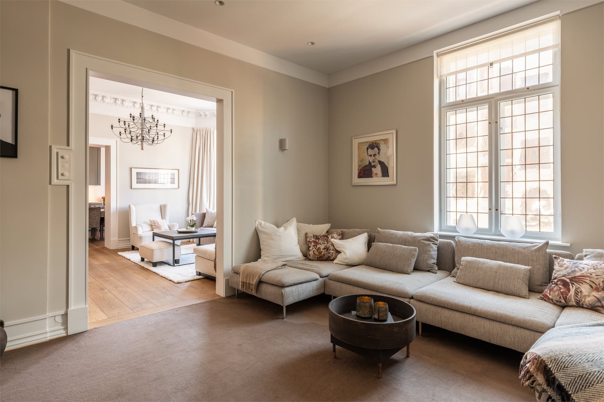 Den tilstøtende stuen fremstår som en mer tilbaketrukket og lun salong, ideell som TV-stue eller bibliotek.