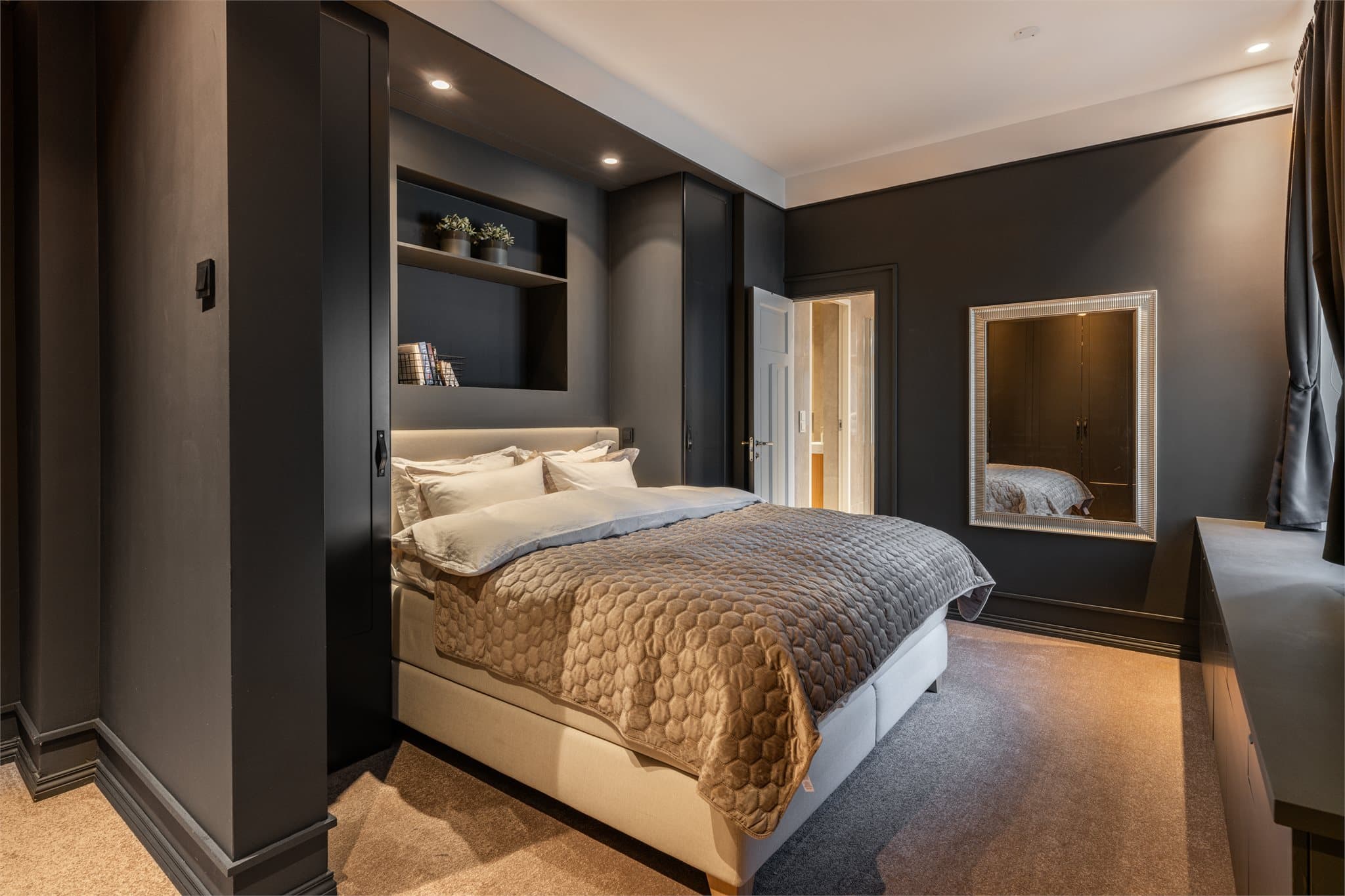 Hovedsoverommet fremstår som en elegant og sofistikert suite, utført i dype, harmoniske fargetoner og med vegg-til-vegg-teppe som tilfører rommet en lun og eksklusiv karakter.