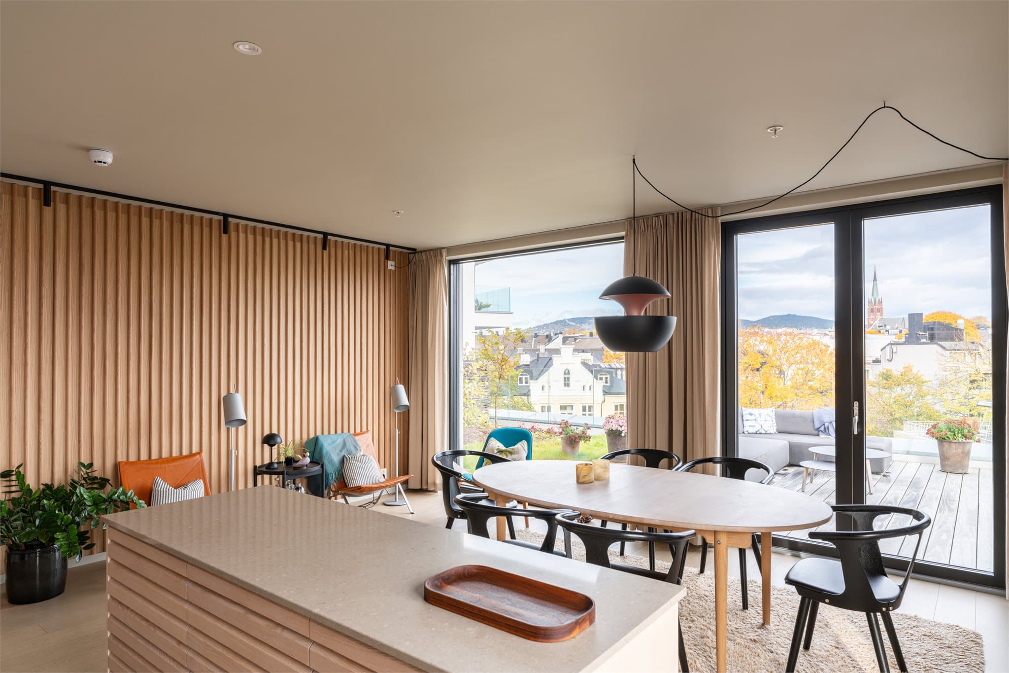 En elegant spilevegg i tre gir rommet karakter og varme, mens store vinduer slipper inn rikelig med dagslys.