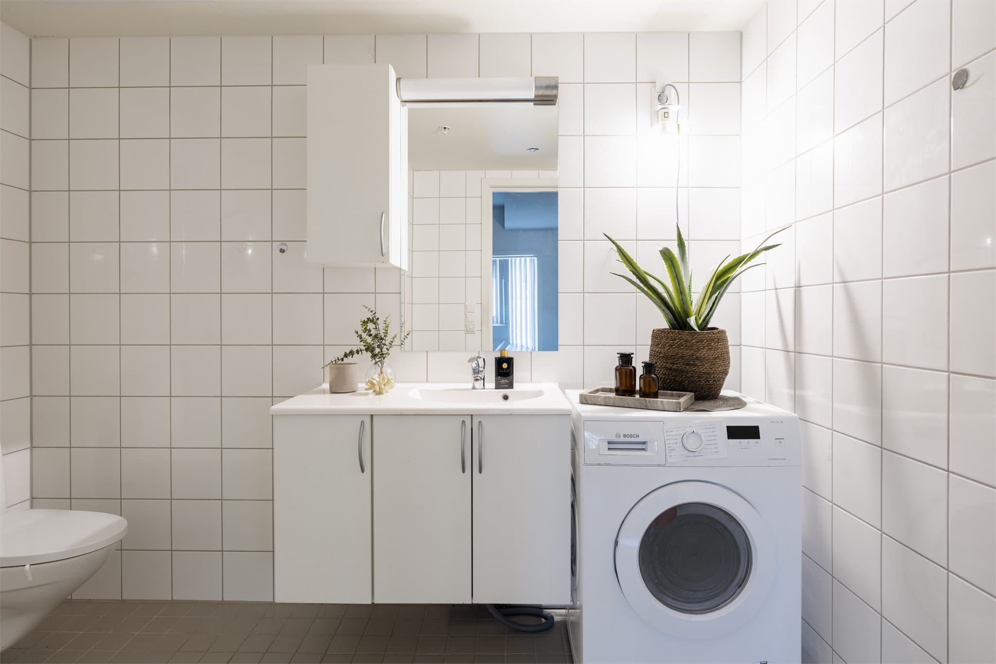 Badet har flislagte vegger, baderomsinnredning med nedfelt servant og opplegg for vaskemaskin.