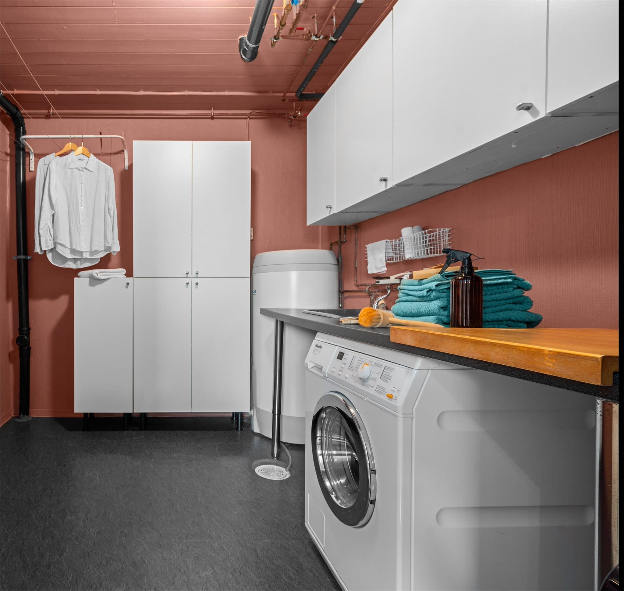 Vaskerom i underetasje med opplegg for vaskemaskin, skap og benk med utslagsvask.