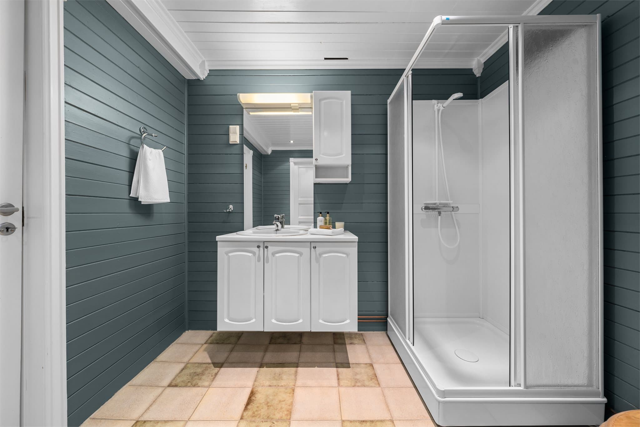 Bad med gulvvarme og innredet med servant på skapseksjon, dusjkabinett og klosett.