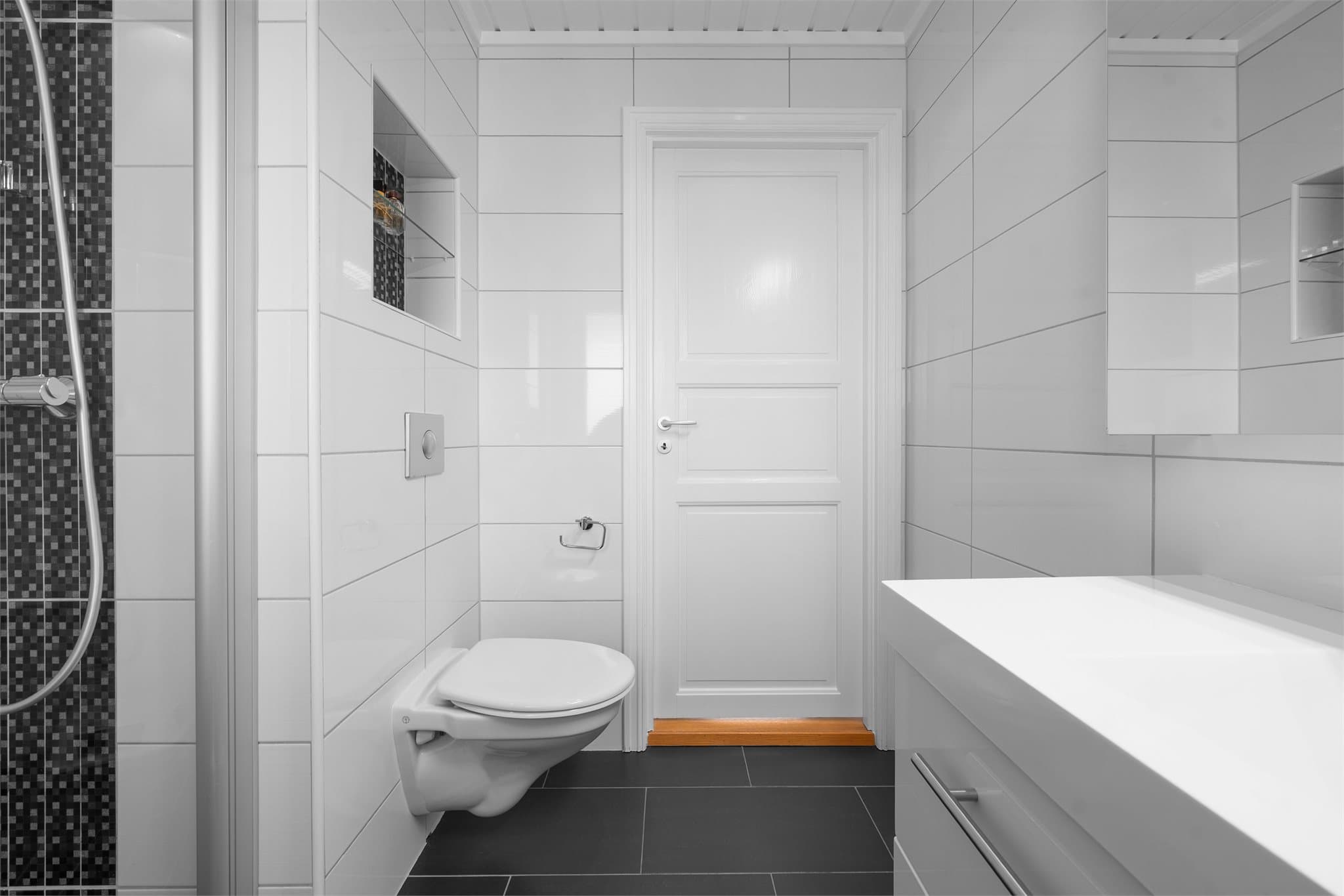 Baderommet har vegghengt toalett, dusjløsning og servant på skuffeseksjon.