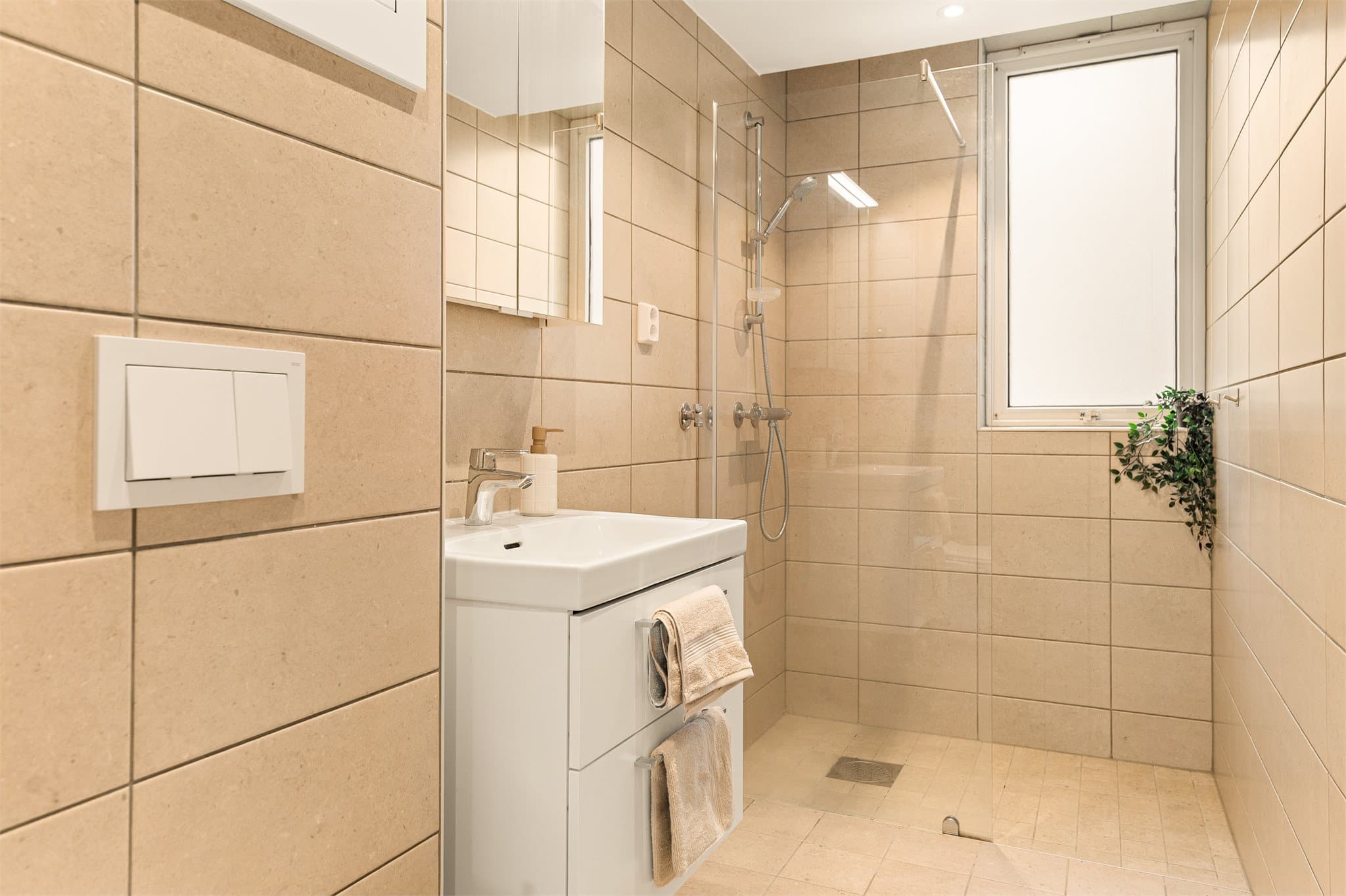 - Badet er innredet med nedfelt servant, dusjvegg, opplegg for vaskemaskin, vegghengt toalett og overskap med speil -