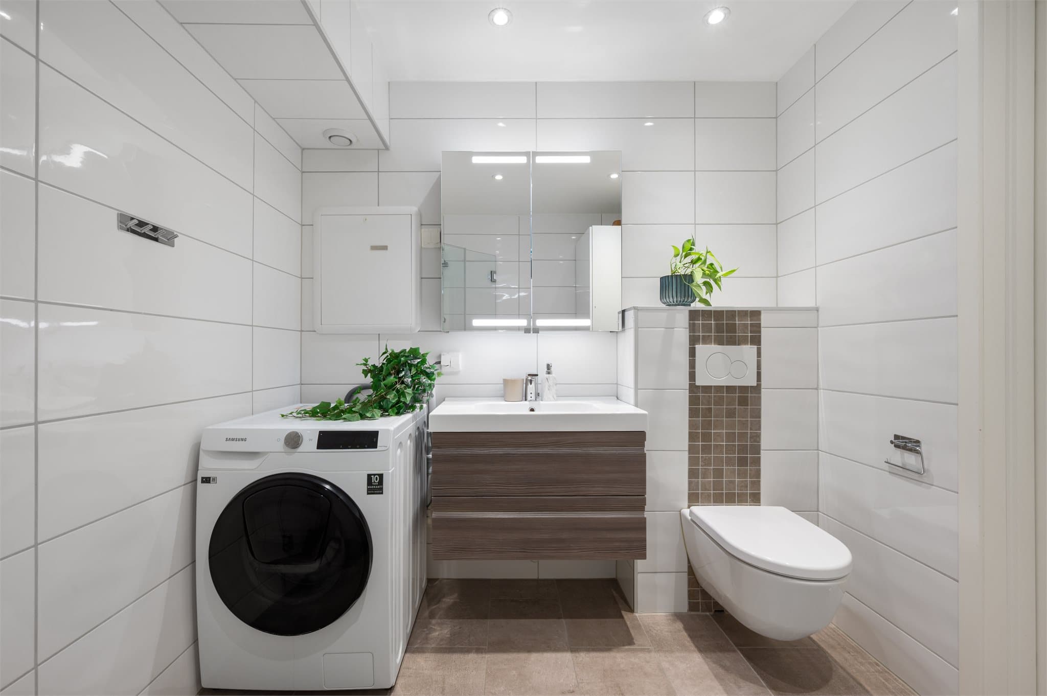 - På badet er det vegghengt toalett, servant med innredning, dusjhjørne og opplegg for vaskemaskin -