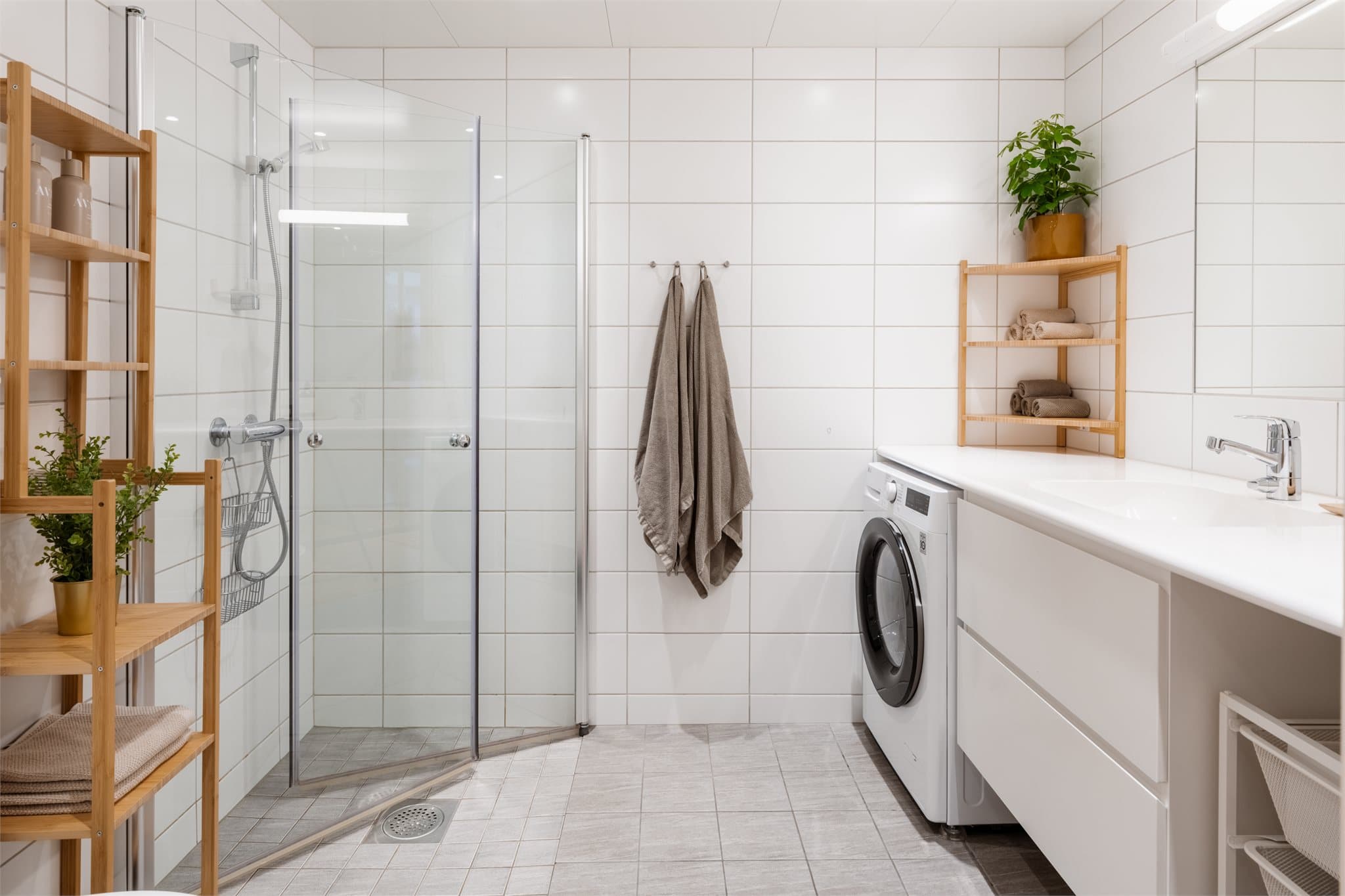 Delikat og flislagt baderom med opplegg for vaskemaskin og tørketrommel under benkeplate.