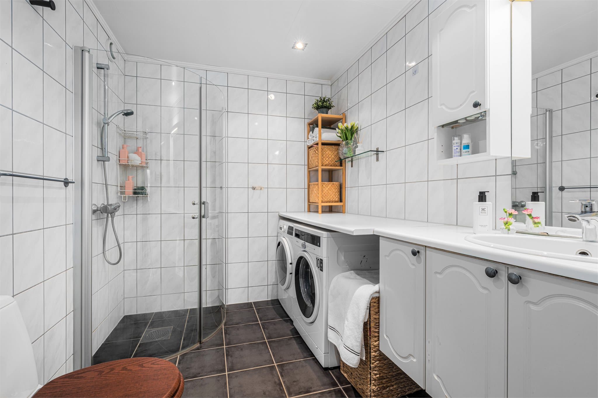 Badet har lyse fliser på veggene og mørkere gulvfliser som gir en fin kontrast. Innfelte spotter i taket sørger for belysning, mens den brede speilflaten over servanten bidrar til romfølelsen.