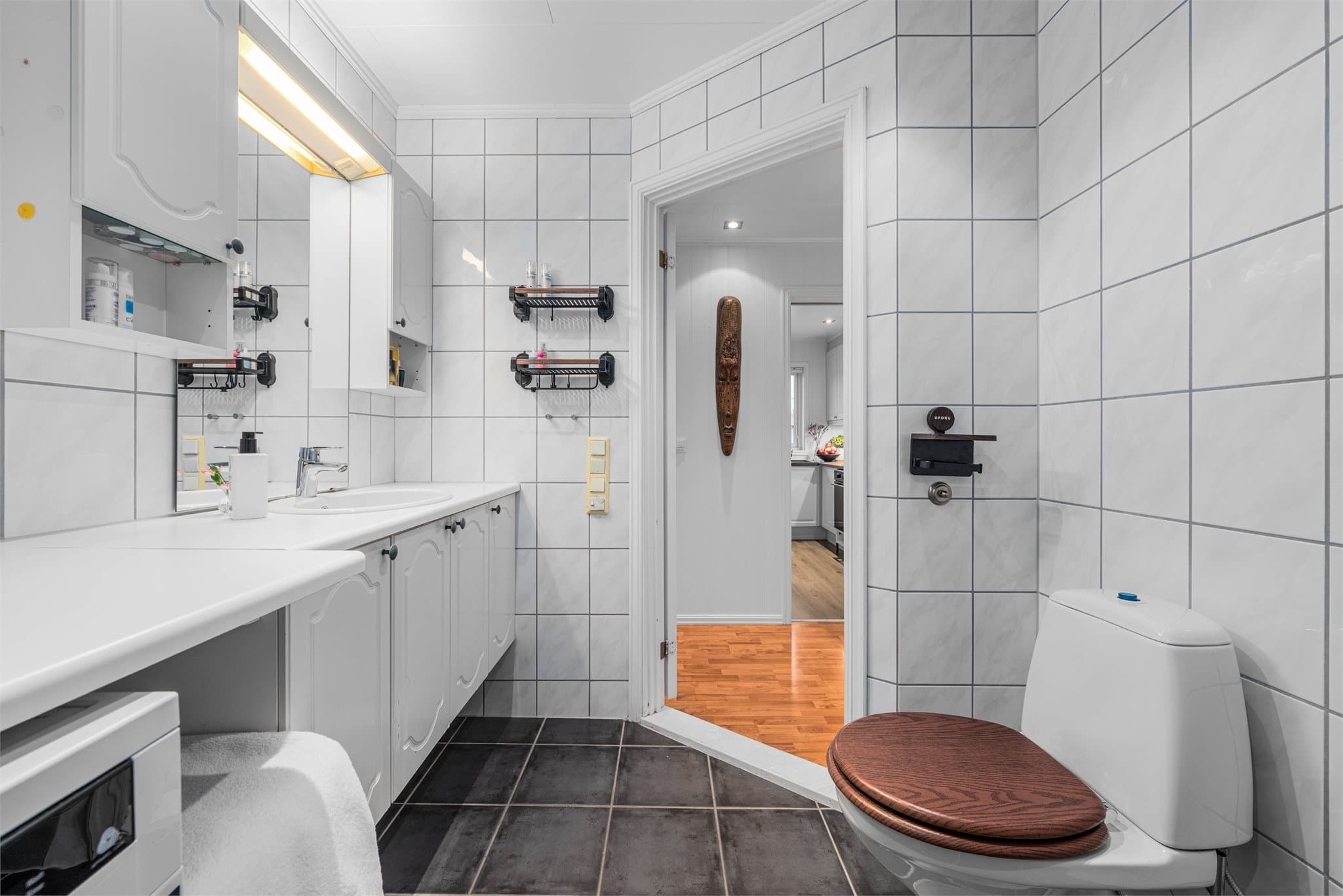 Badet er innredet med dusjhjørne med glassdører, gulvstående toalett og servant med skapplass til håndklær og toalettsaker.