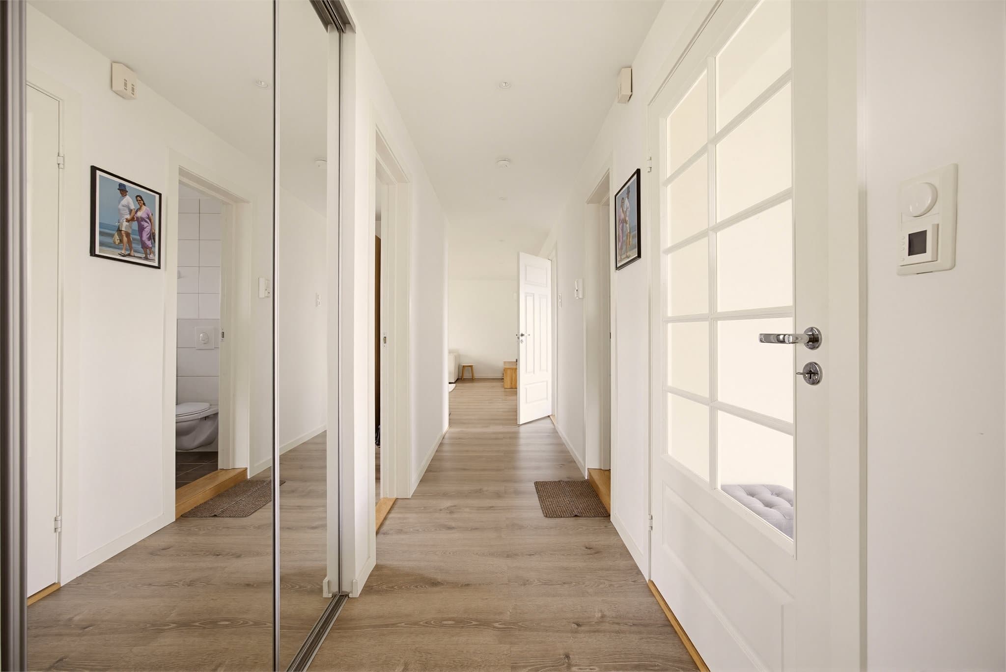 En dør med glassfelt skiller gangen og entréen. Gangen byr på stor skyvedørsgarderobe med plass til alle ytterklær og sko.