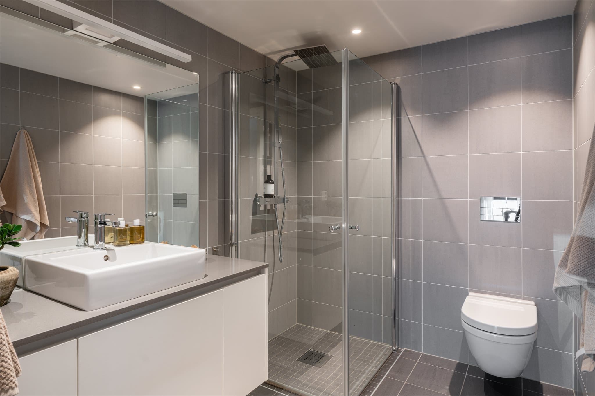 Badet er innredet med servant med tilhørende innredning, dusjhjørne med svingbare glassdører og vegghengt toalett. Badet har balansert ventilasjon.