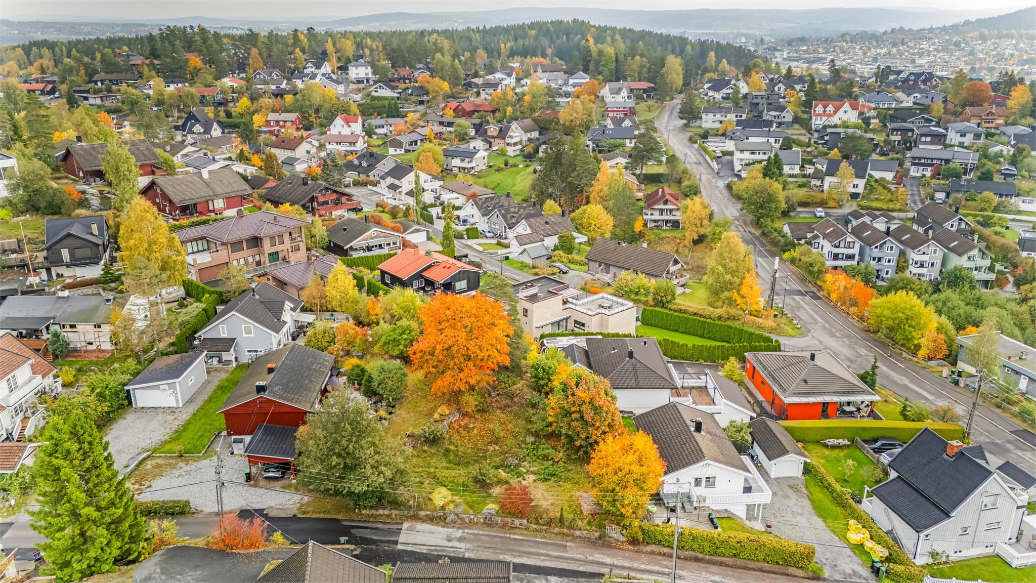 Tomten har egen innkjøring, plen, naturlige terrengnivåer, flere trær og busker.
