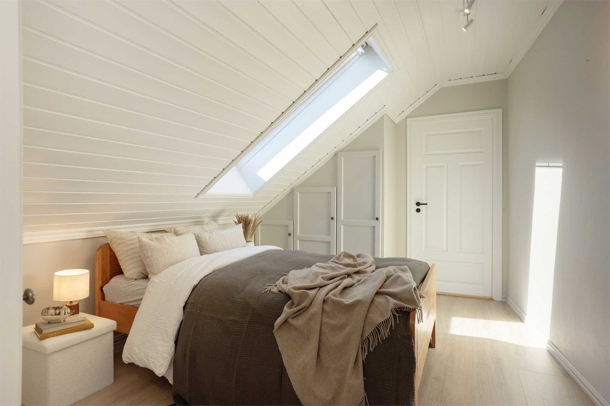 Hovedsoverommet har skråtak med hvitmalt panel og takvindu.