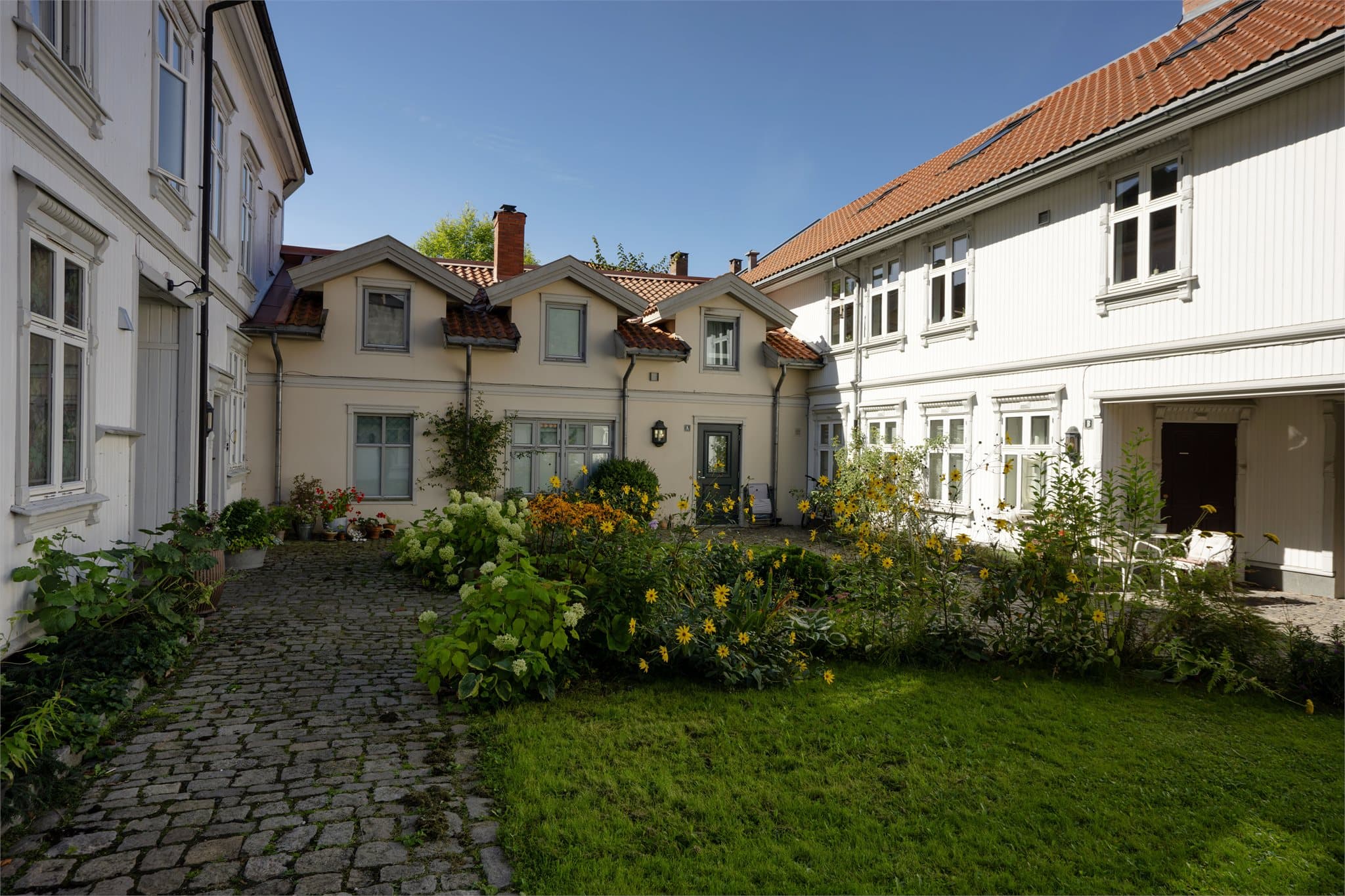 Idyllisk og bilfritt tun med gressplen og brosteinsganger.