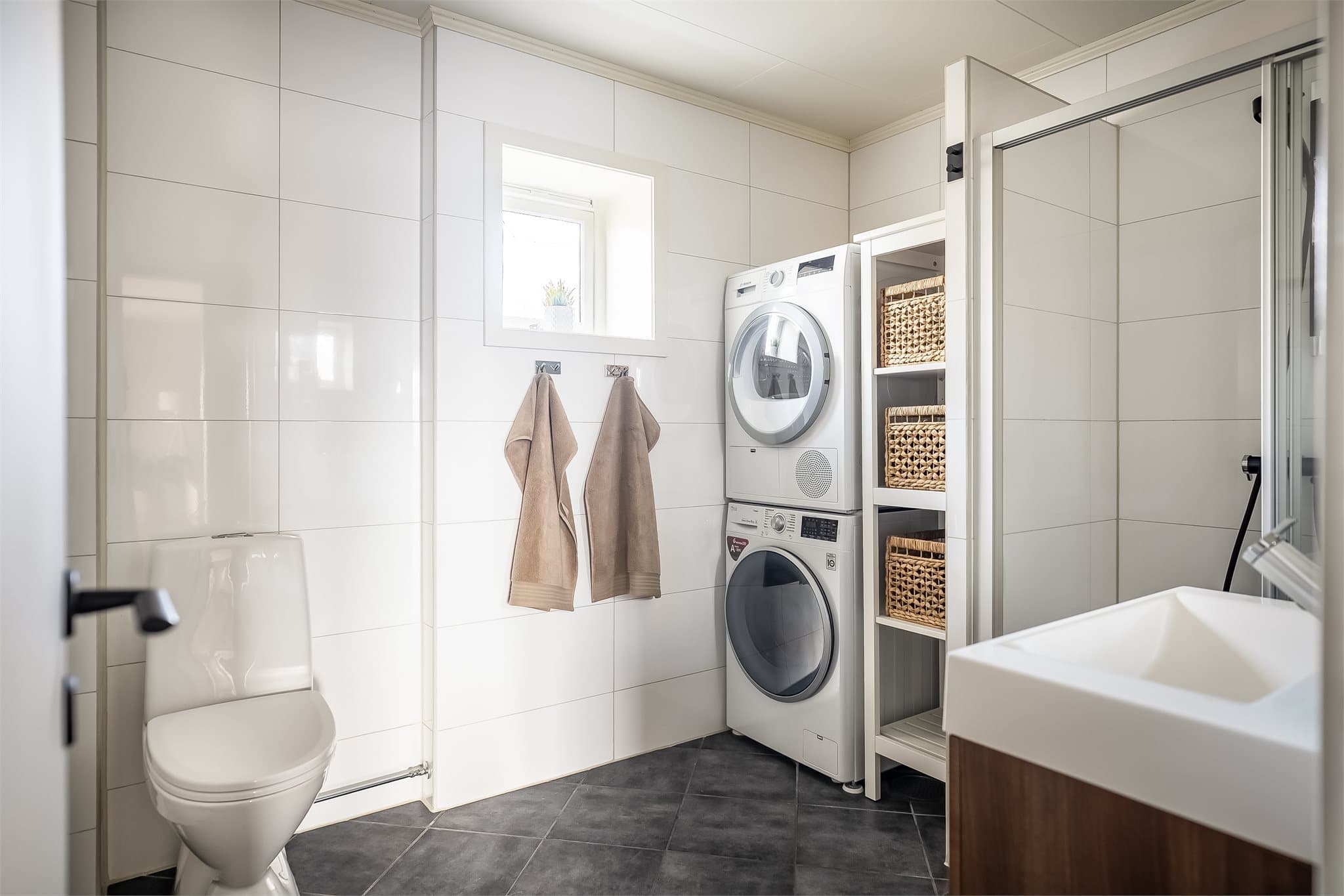 Lyst og moderne baderom utstyrt med servantinnredning, speil, toalett og dusjnisje.