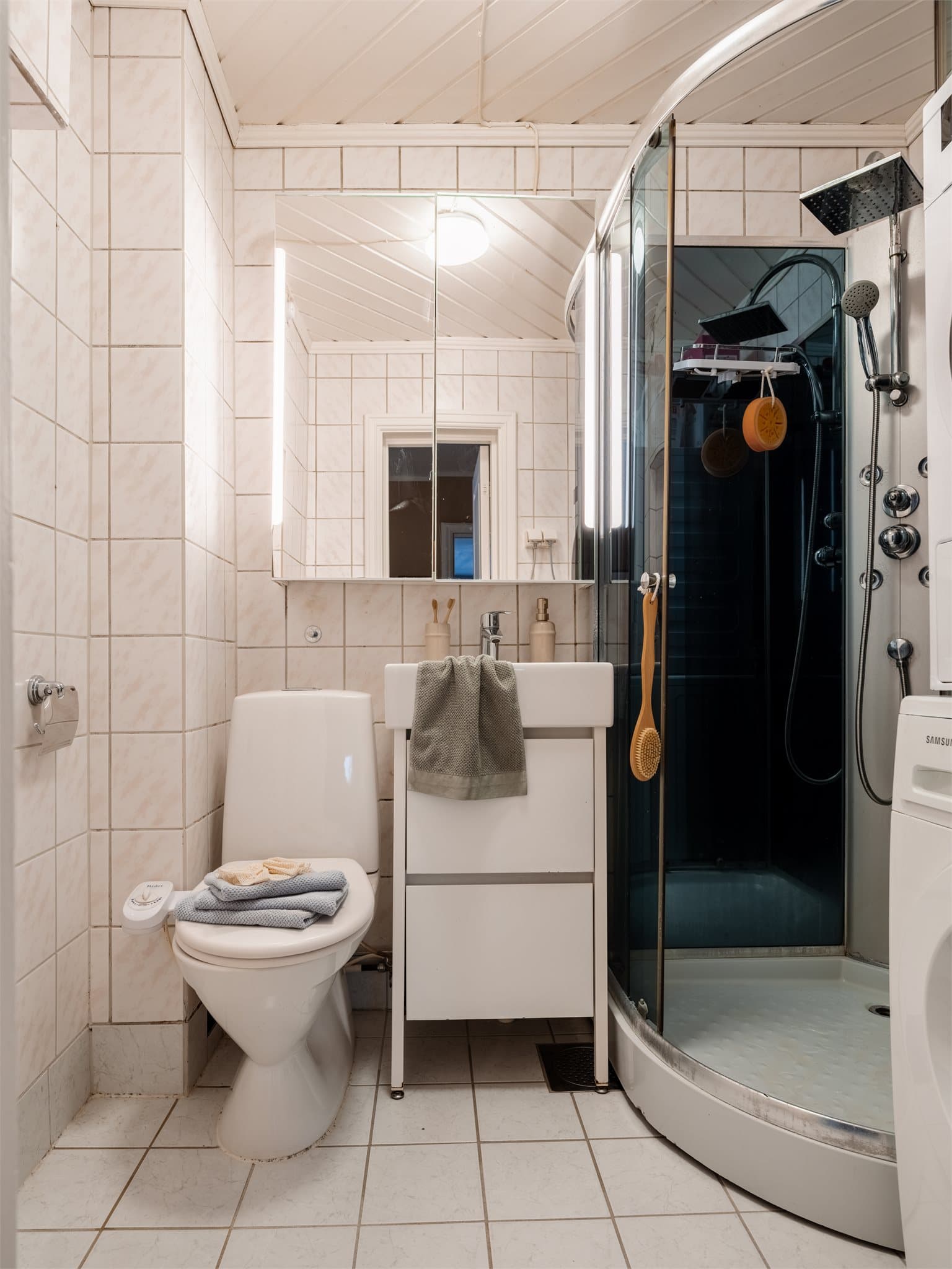 Et lyst, flislagt baderom med varme i gulvet og opplegg for vaskemaskin/tørketrommel.