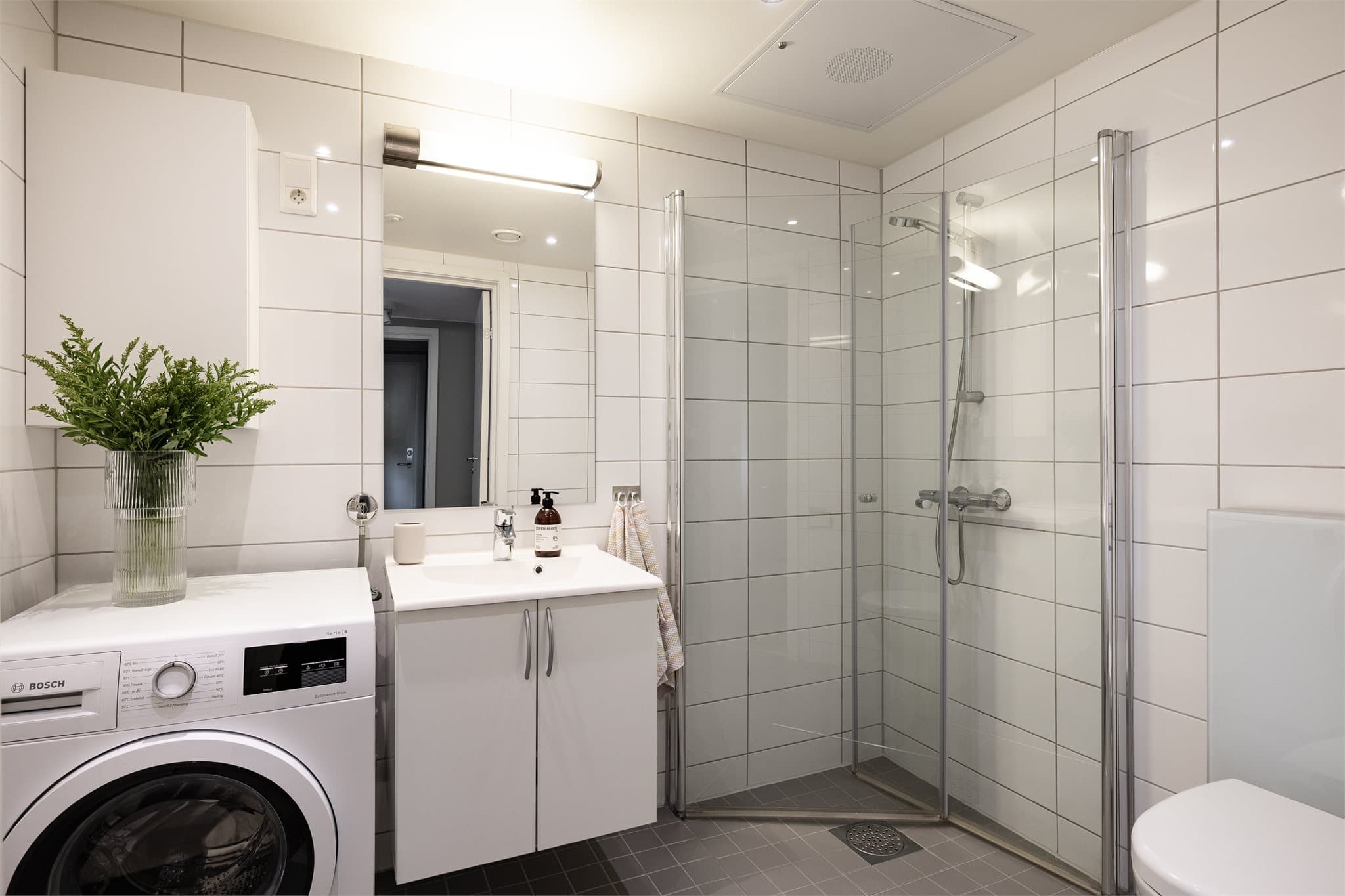 Et lyst og flislagt baderom med gulvvarme og downlights i taket.