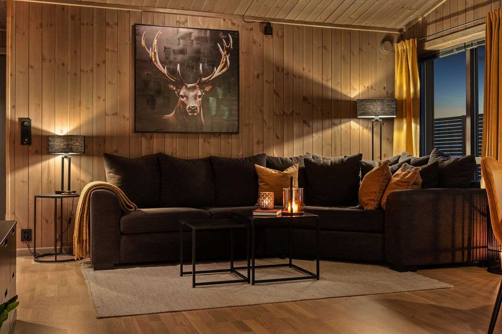 Hytta ønsker deg velkommen inn i en lys og behagelig stue med parkettgulv som gir rommet et elegant og tidløst uttrykk. De lasurbeisede panelkledde veggene tilfører en lun, naturlig stemning og perfekt balanse mellom moderne og klassisk hyttedesign.