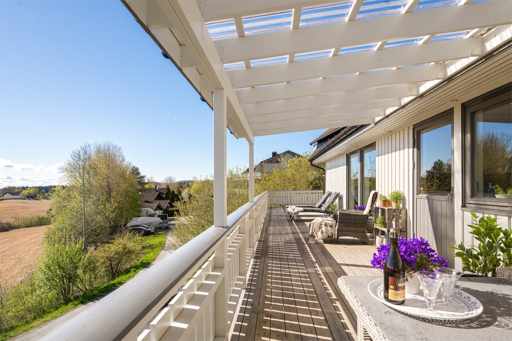 Den store verandaen fungerer som en naturlig forlengelse av boligens oppholdsrom og gir rikelig med plass til både spisegrupper, loungeområder og rolige solkroker. Pergolaen ved kjøkkenutgangen skaper en lun og stemningsfull ramme rundt uteplassen.