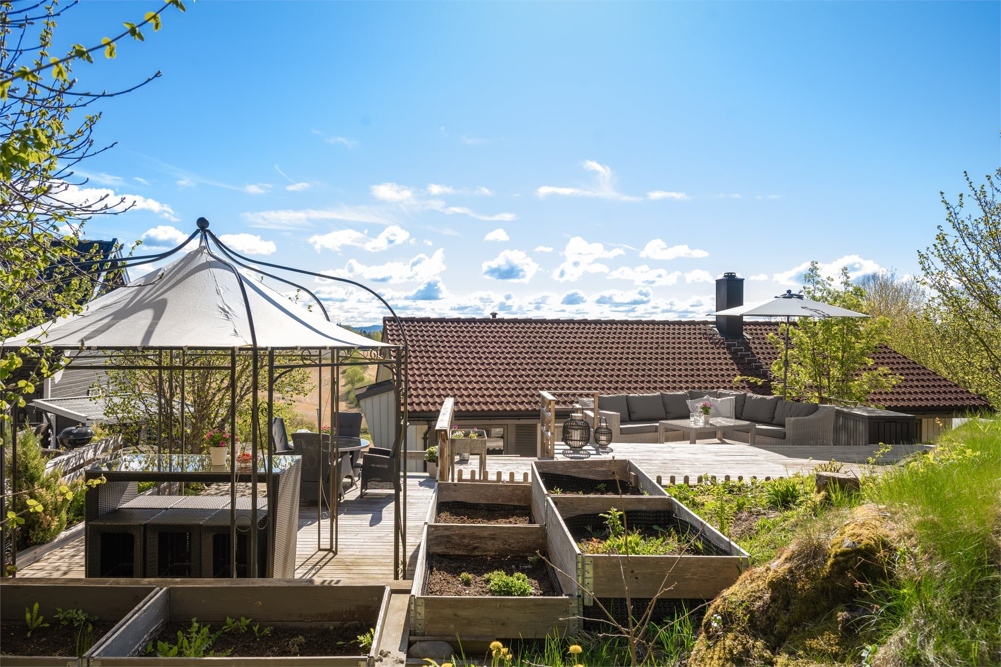 En skjermet og solrik uteoase hvor flere flotte terrasseplattinger sys sømløst og naturlig inn i det vakre terrenget. Her kan sommerdagene nytes i rolige omgivelser med god plass til både avslapning og hyggelige sammenkomster.