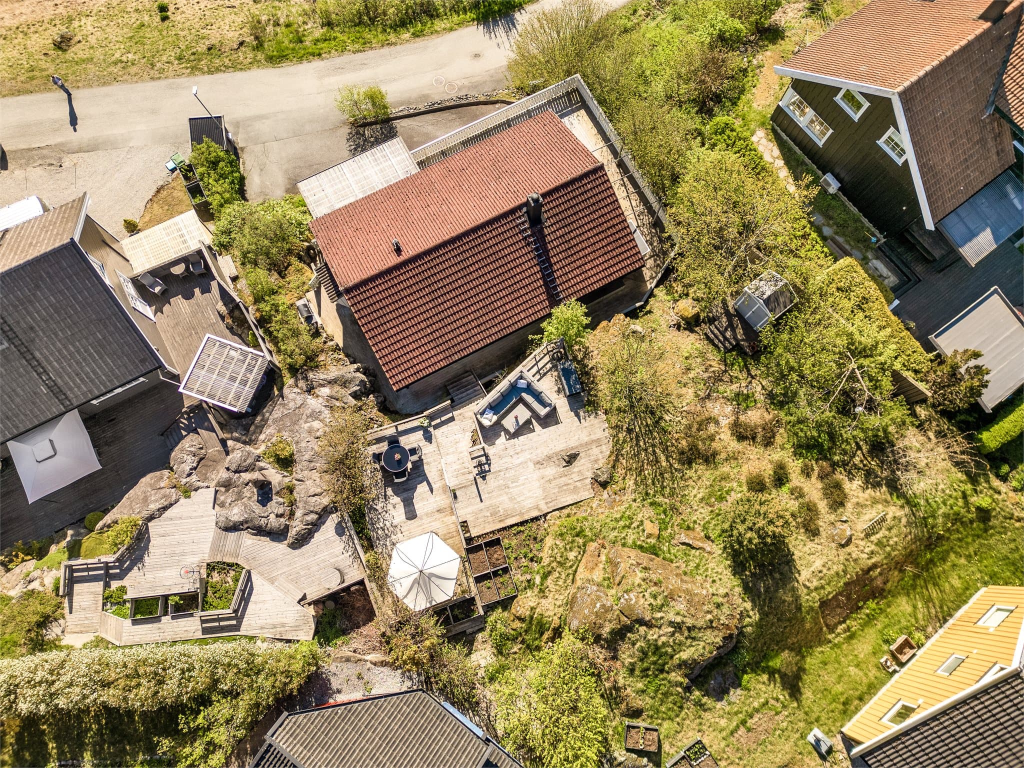 Fra luften ser man tydelig de flotte uteområdene med flere terrasser og lune oppholdssoner som glir naturlig inn i terrenget bak boligen.